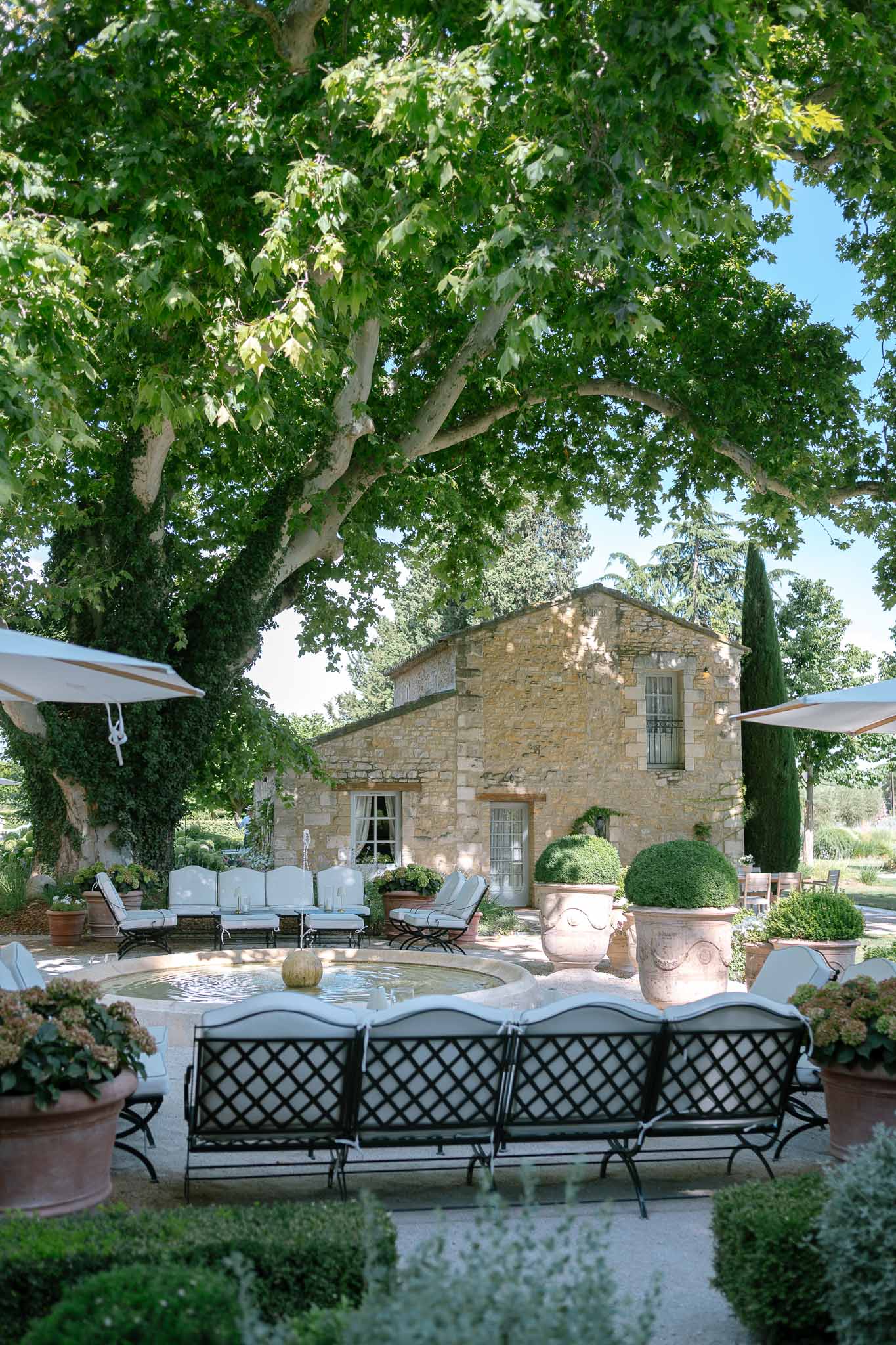 Provencal stone mas courtyard with iron benches, stone fountain, topiary urns, and cypress trees