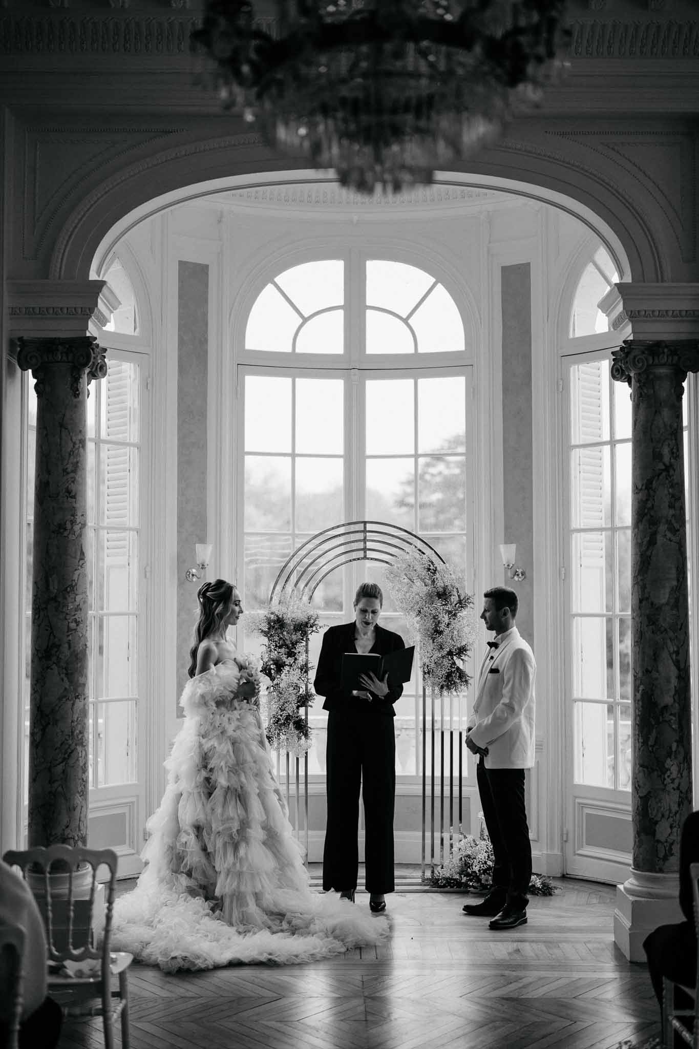 Black and white ceremony in ballroom with ruffled tulle gown, gypsophila circle arch, and herringbone parquet floor