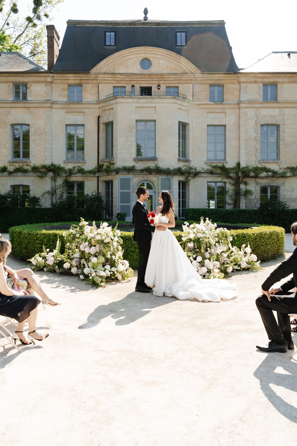 Couple at altar before cream chateau with espaliered walls and white peony ground installation