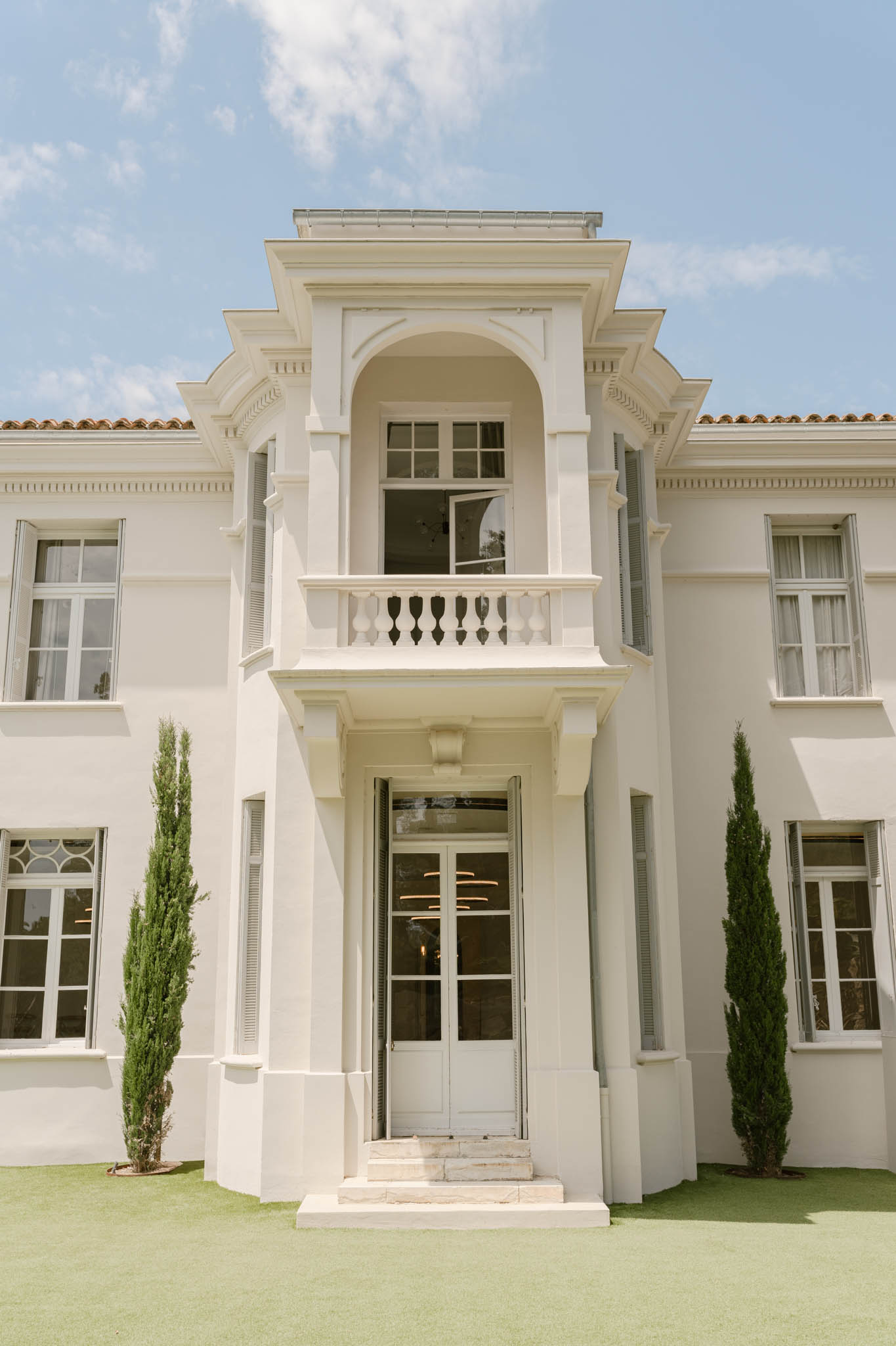 White rendered villa with balustraded balcony flanked by Italian cypress trees