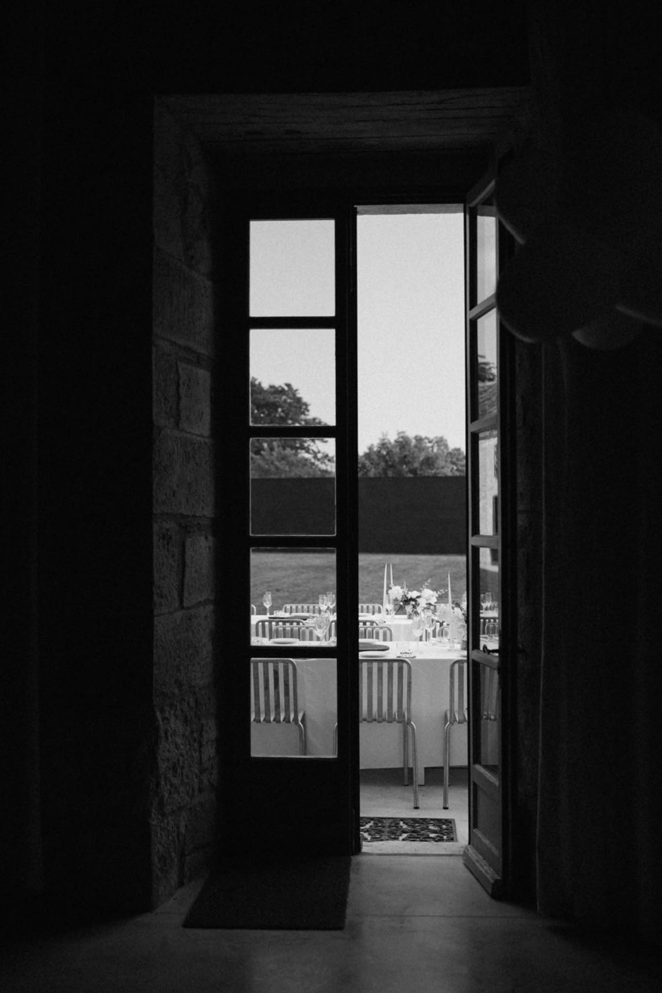 View through stone doorway to outdoor reception table set with glasses and candles in B&W