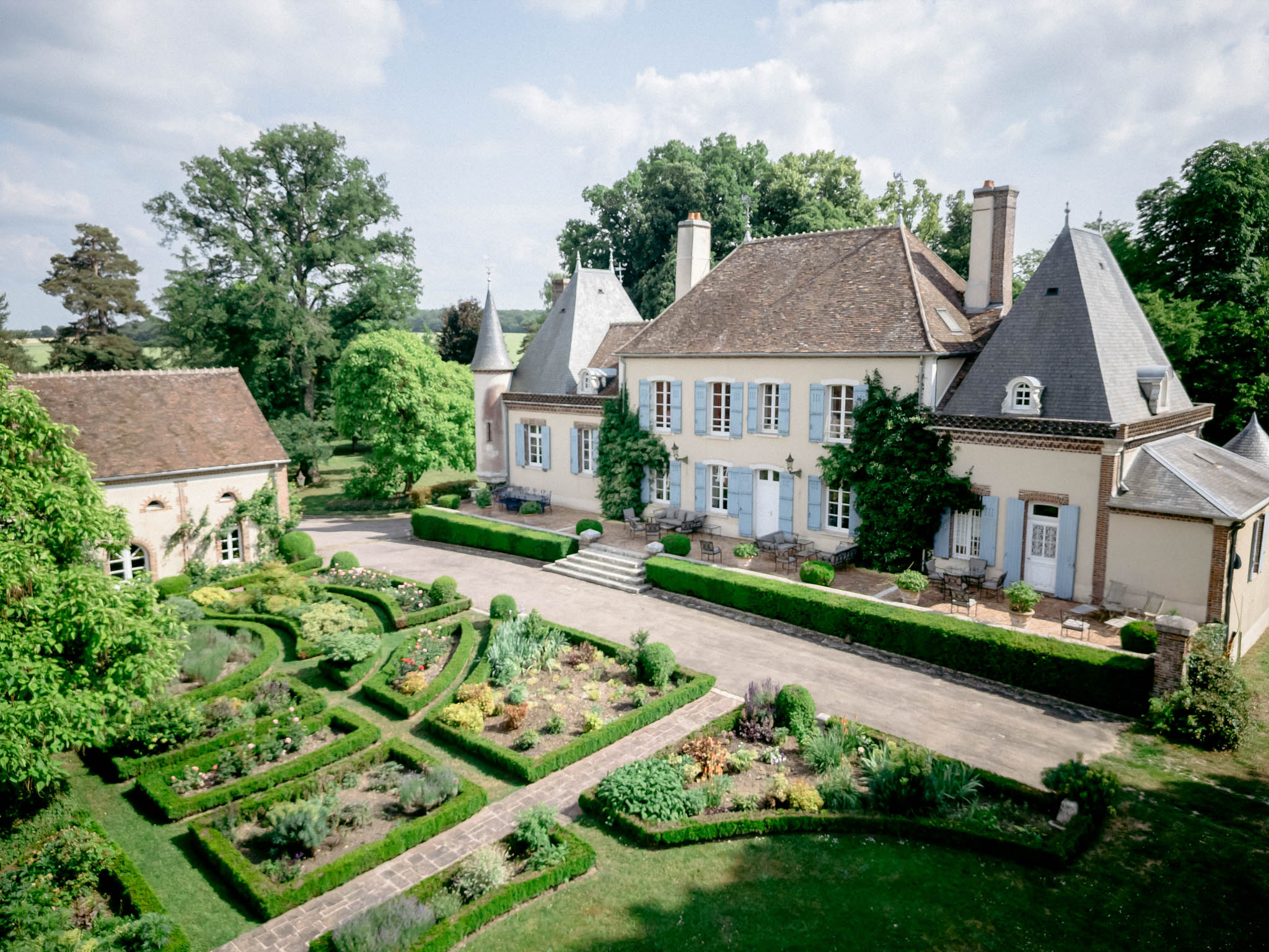 Aerial view of cream-rendered French manor house with slate roofs, parterre garden, and box hedging