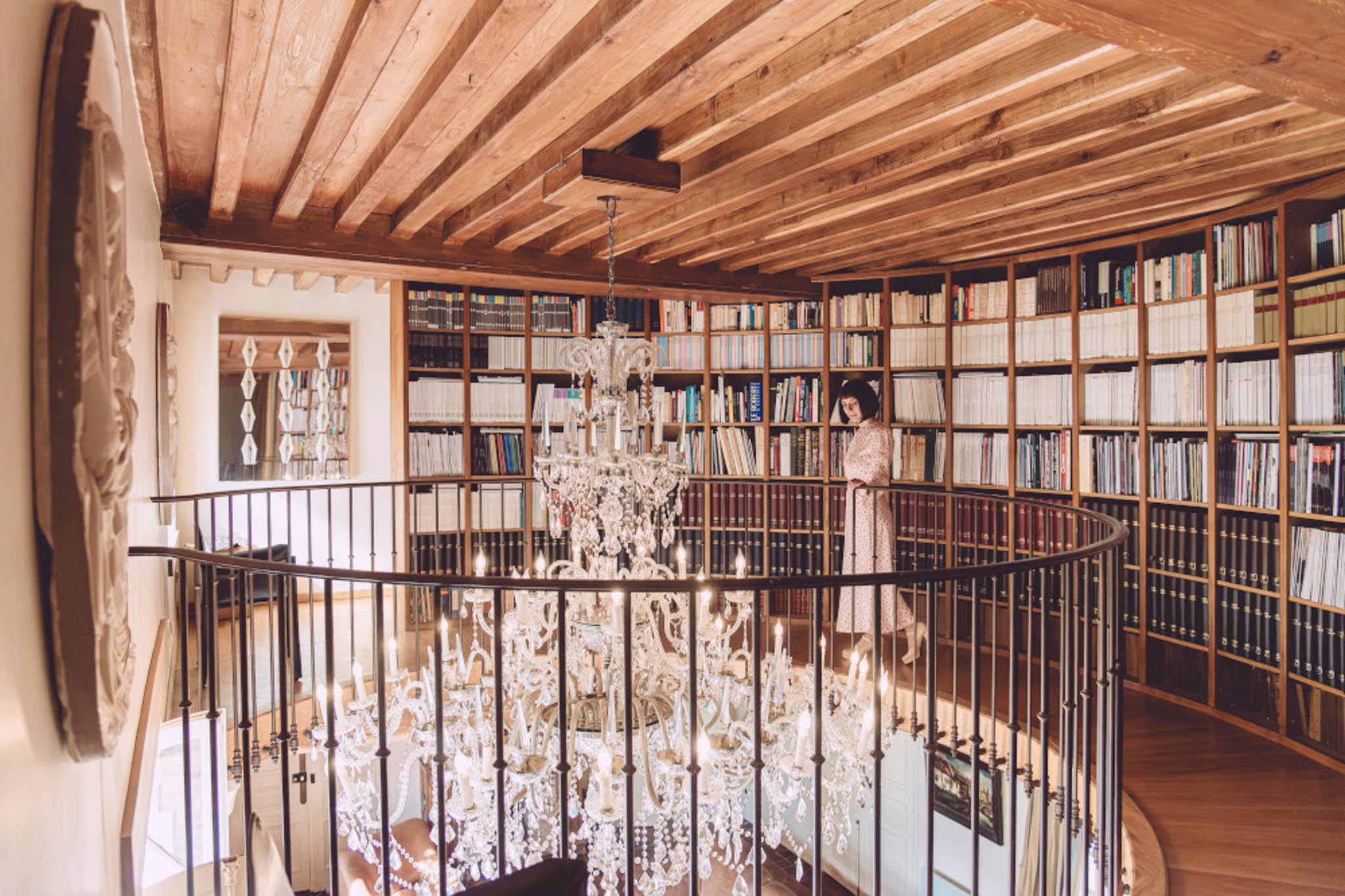 Curved mezzanine library with floor-to-ceiling bookshelves and tiered crystal chandelier