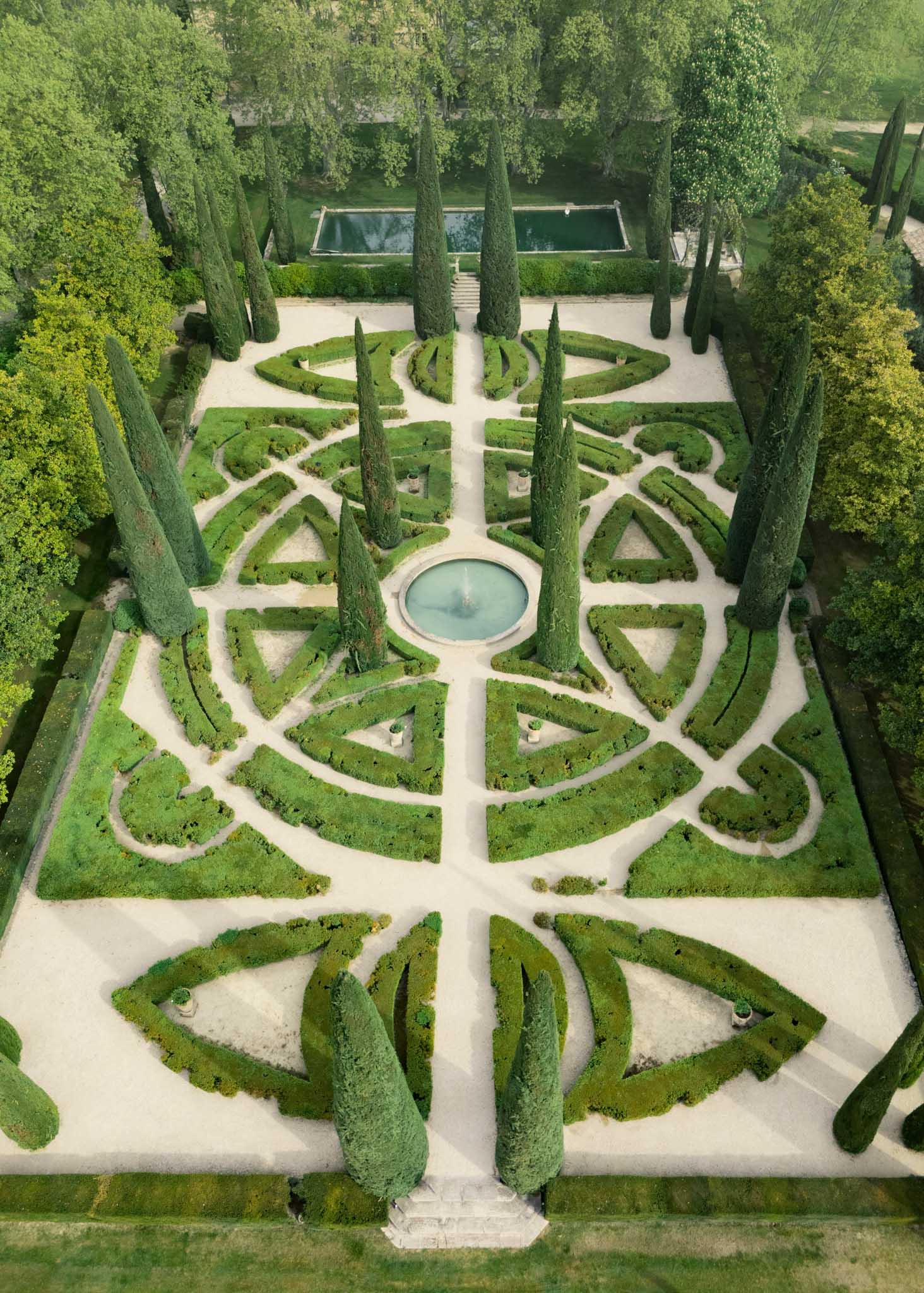 Aerial formal French parterre garden with geometric boxwood hedges central fountain cypress trees and reflecting pool