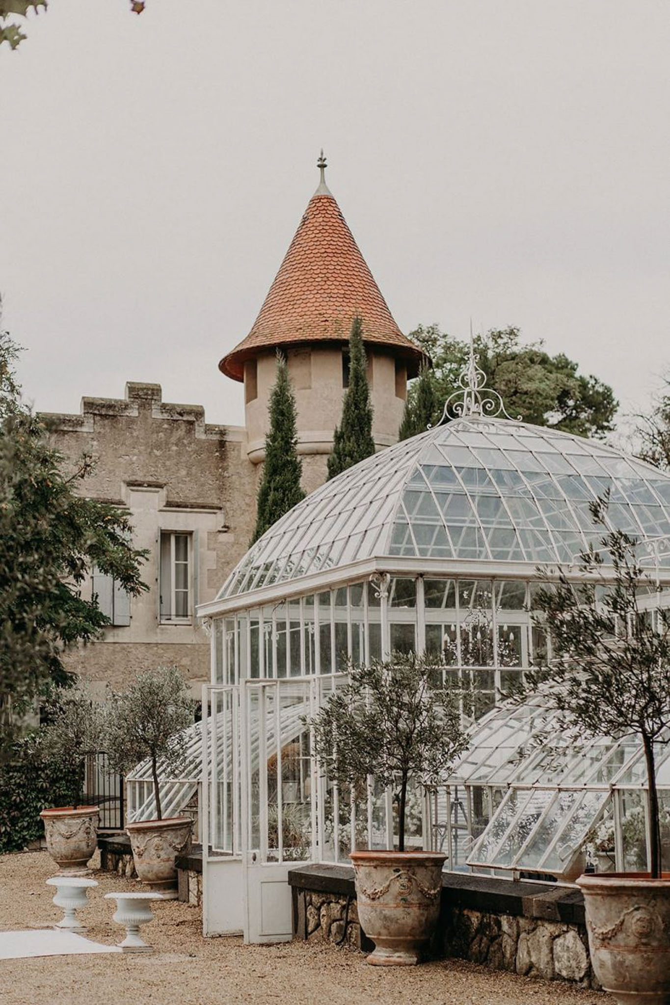 Victorian glass greenhouse with white iron dome beside chateau tower on gravel courtyard