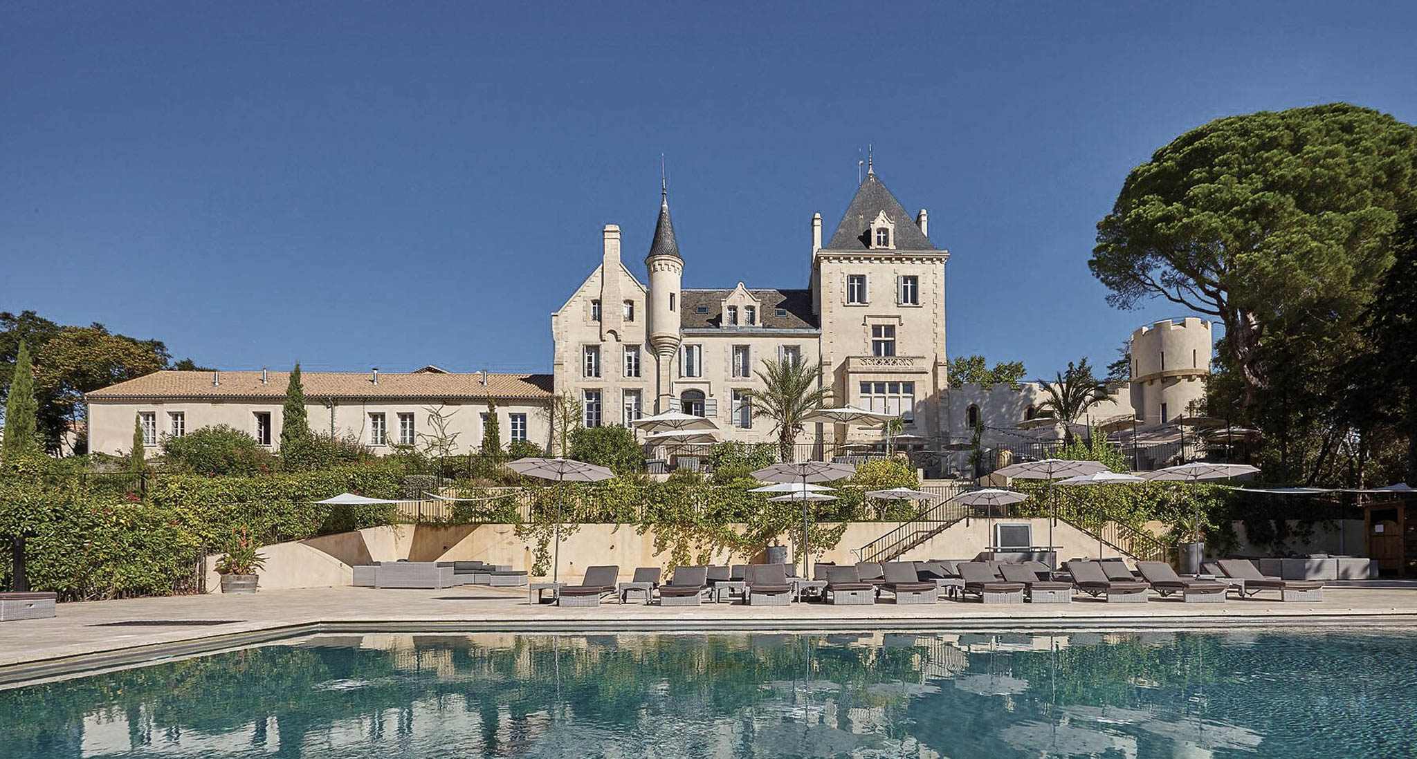 Chateau Les Carrasses exterior with limestone turrets, slate roofs, and poolside sun loungers