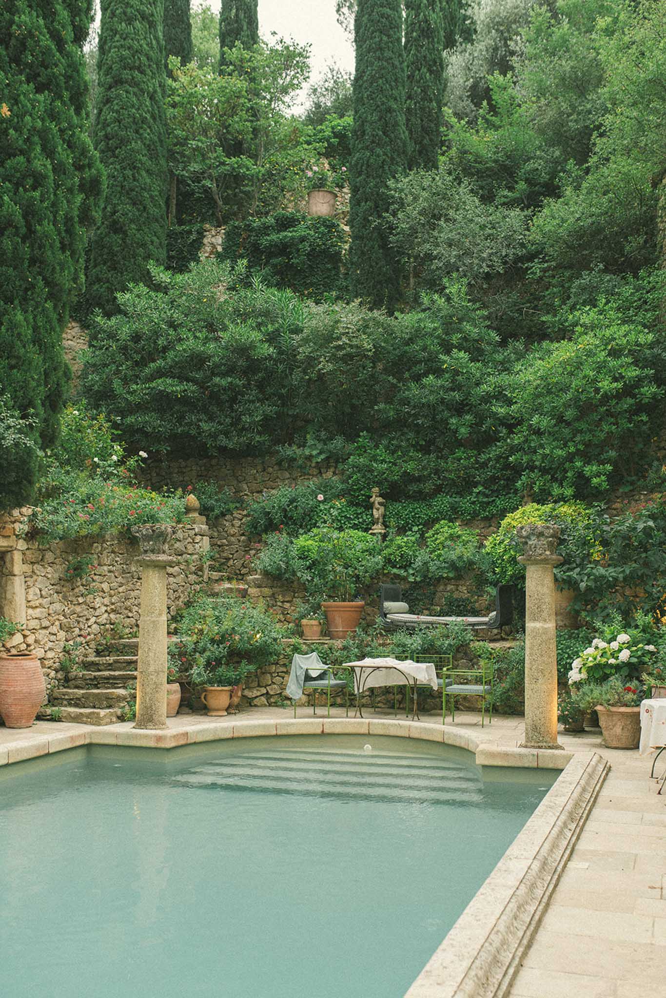 Rectangular pool with stone columns at a Provencal estate, surrounded by terracotta urns, hydrangeas, and cypress trees