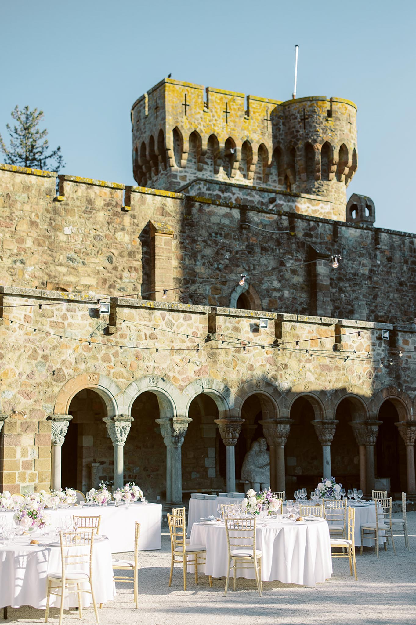 Round tables with gold Chiavari chairs and blush florals in medieval castle courtyard with arcade