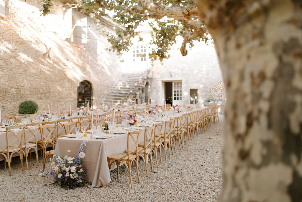 Banquet tables with dusty blue and blush dahlias under string lights in stone courtyard with arched doorways