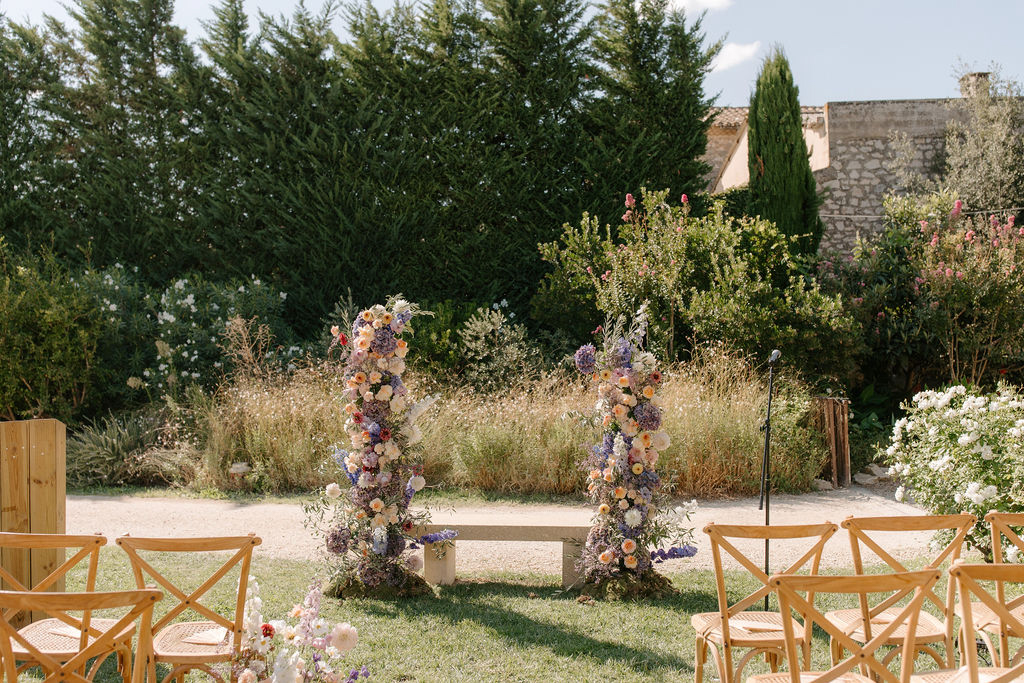 Outdoor ceremony setup with tall floral columns of peach roses and purple delphinium flanking stone altar