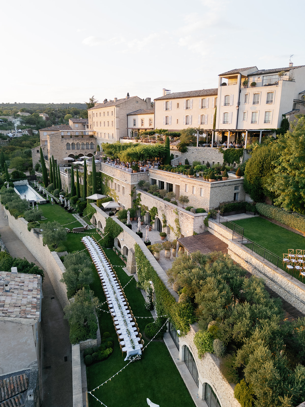 Aerial view of Provencal stone property with banquet tables, fairy lights, and terraced gardens set for reception