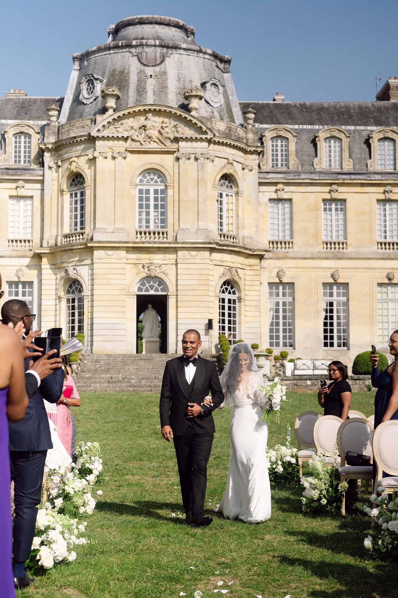 Bride and groom walk up the aisle after outdoor ceremony with Baroque chateau facade behind them