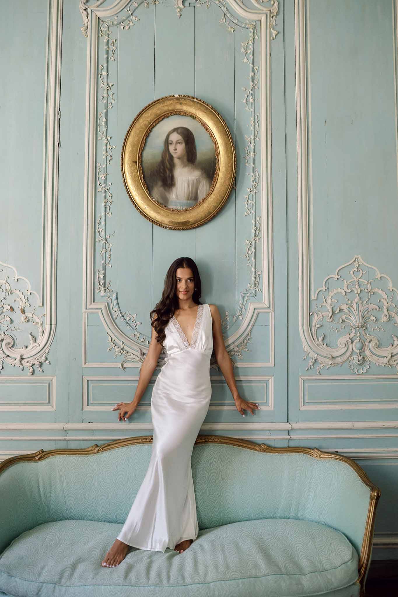 Bride in ivory satin slip gown on mint-blue Louis XVI canape beneath gilt-framed portrait in chateau salon