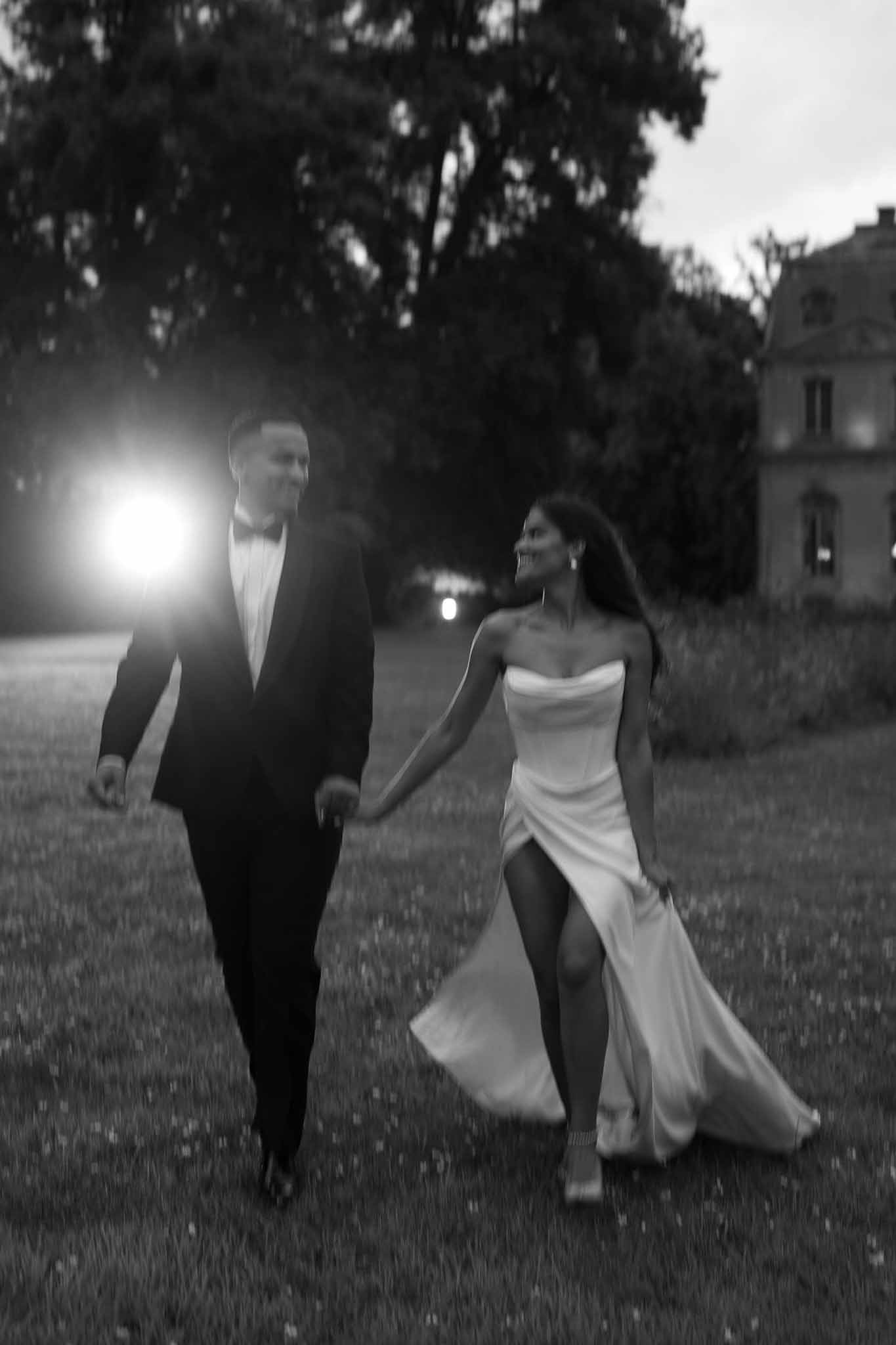 Black and white couple walking across lawn at dusk with lens flare and motion blur at chateau grounds