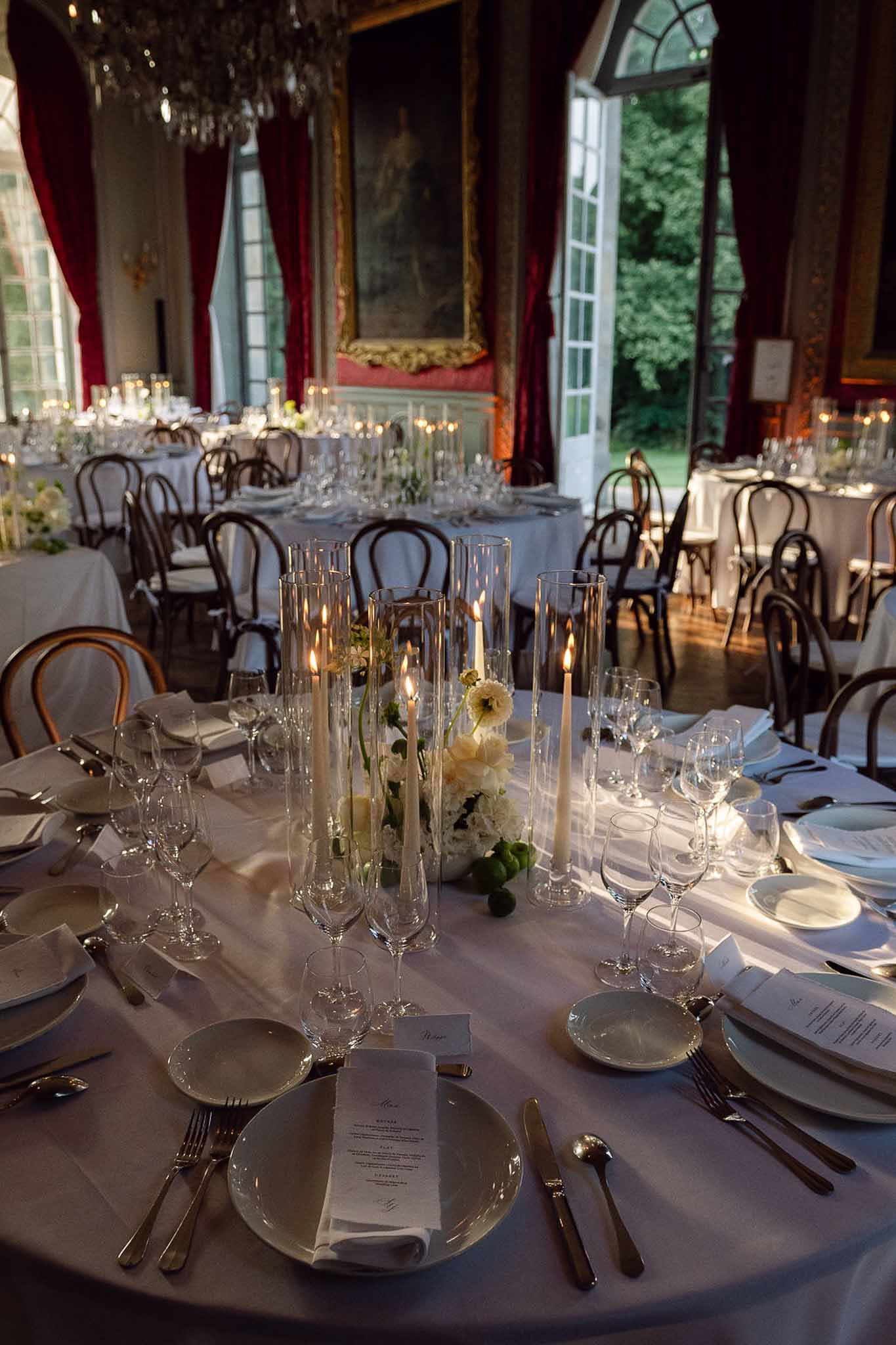Chateau ballroom wedding reception with round tables, ivory floral centerpieces, candles, and crystal chandelier