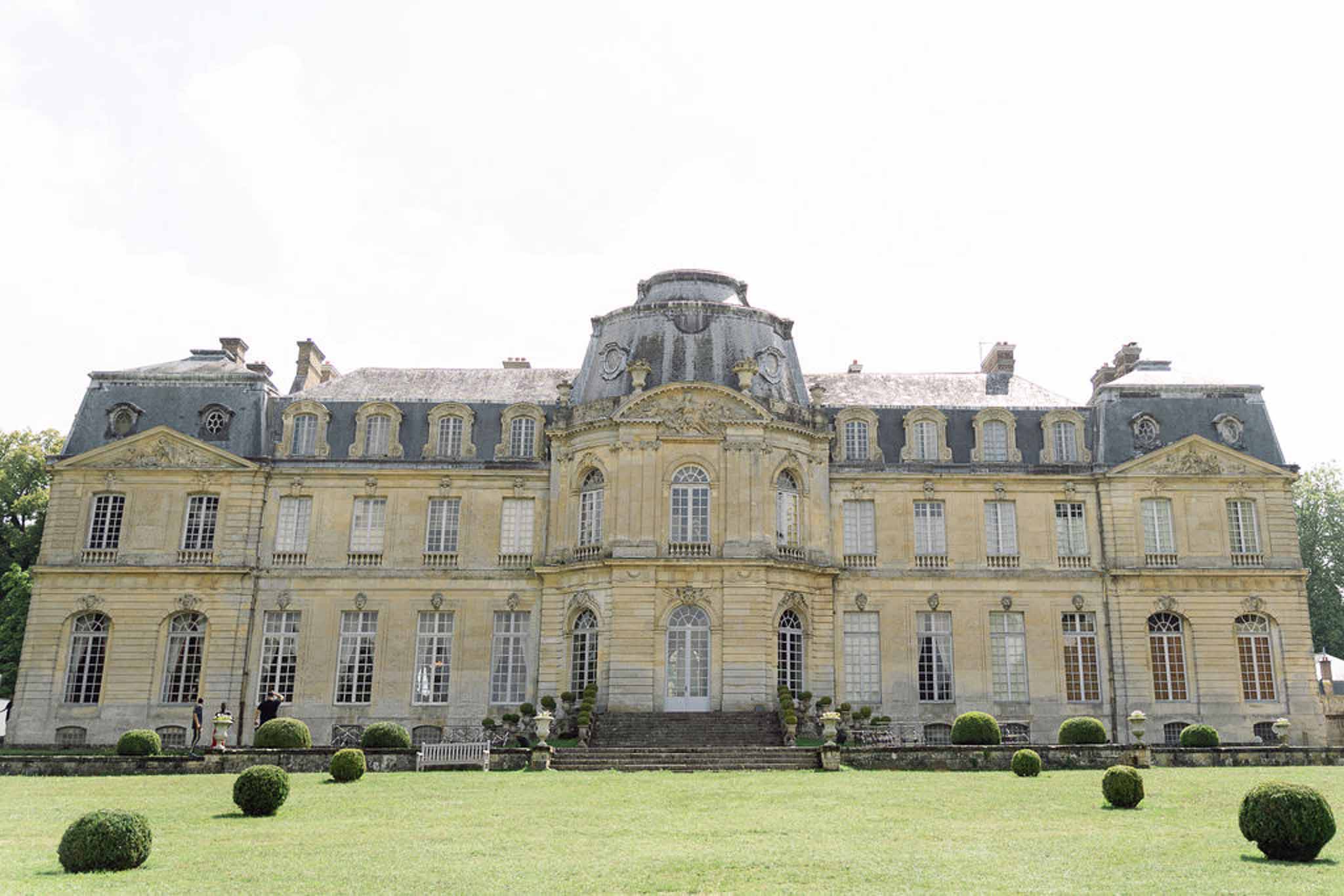 Classical limestone chateau with mansard roof, domed pavilion, and spherical topiary on terrace