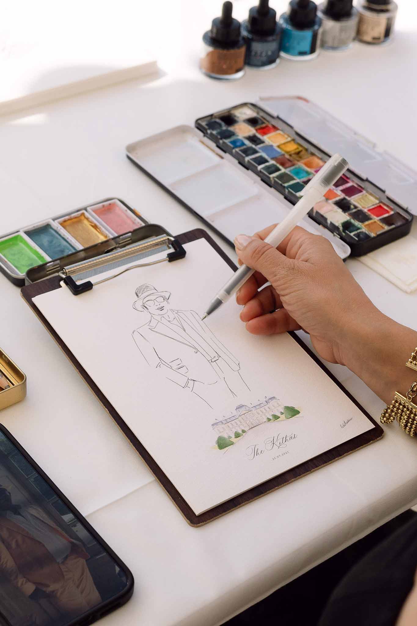 Close-up of live wedding illustrator drawing guest portrait with watercolors and fine-liner pen at reception