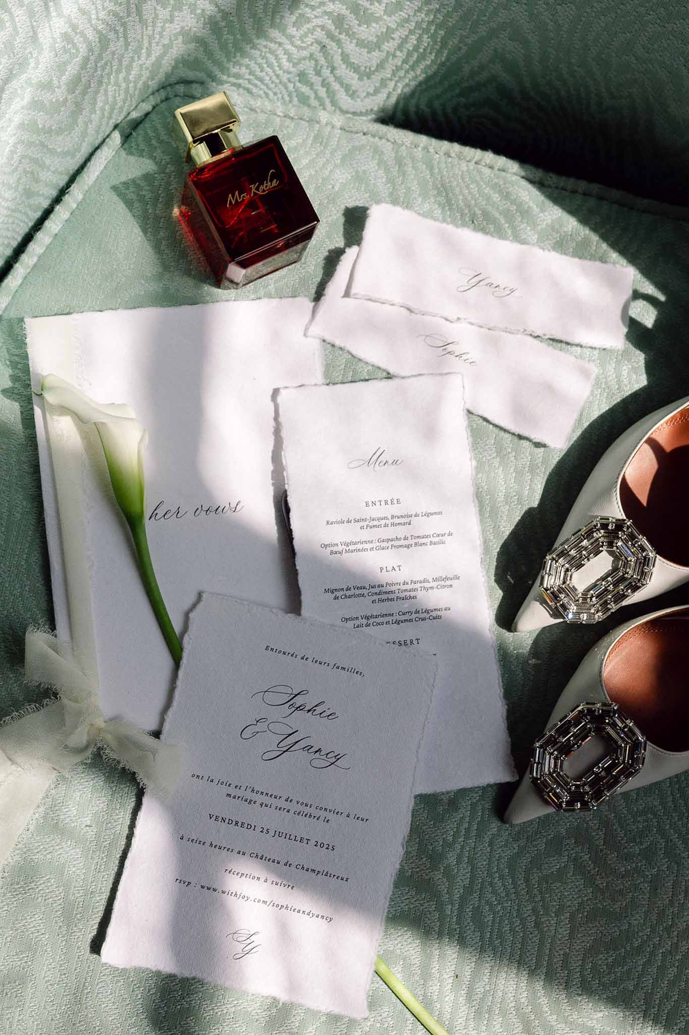 Stationery suite with pale blue invitation, vow booklet, crystal-toe heels, and calla lily on sage moire fabric