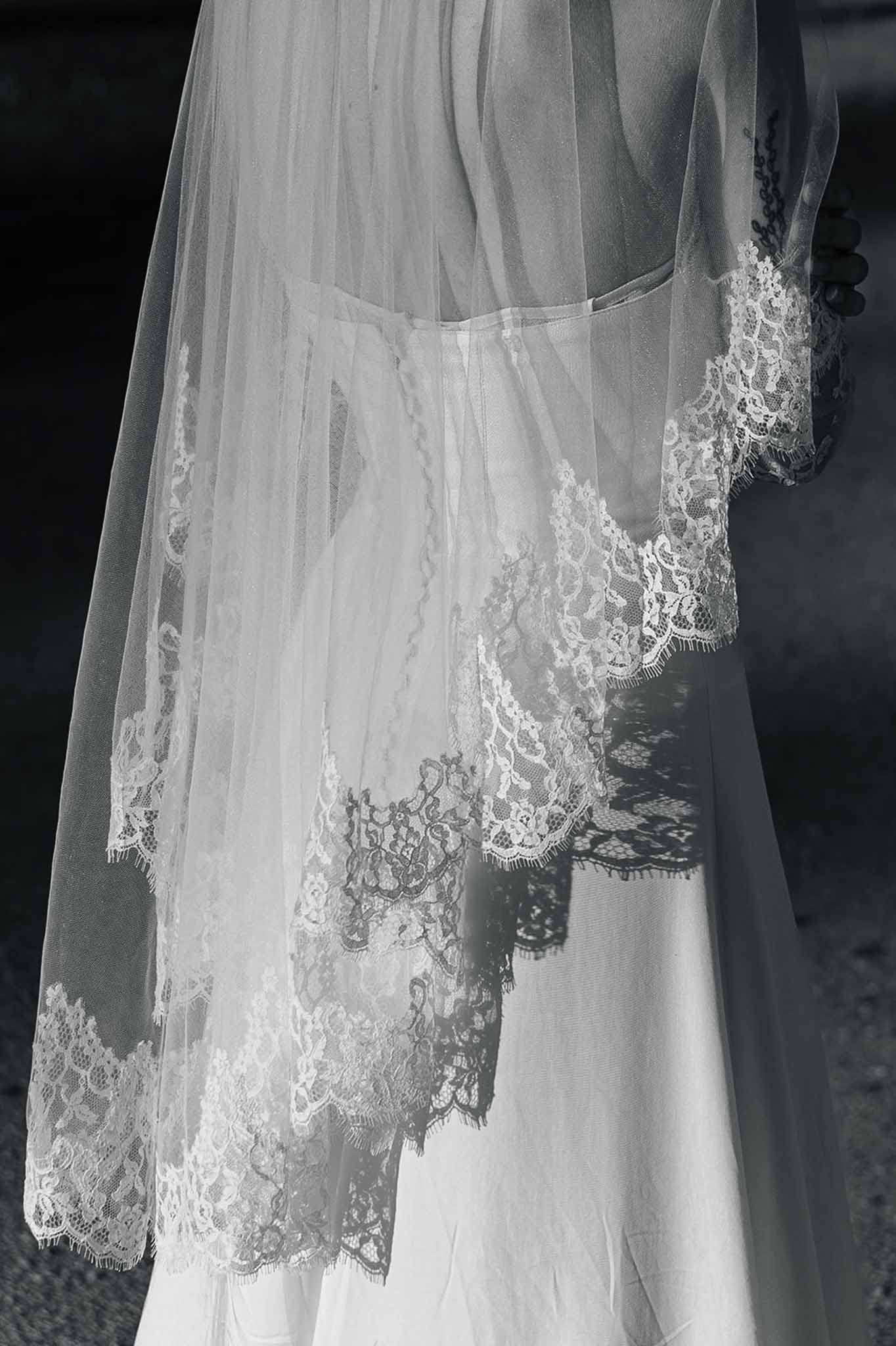 Black and white detail of Chantilly lace veil edge casting shadow pattern on wedding gown