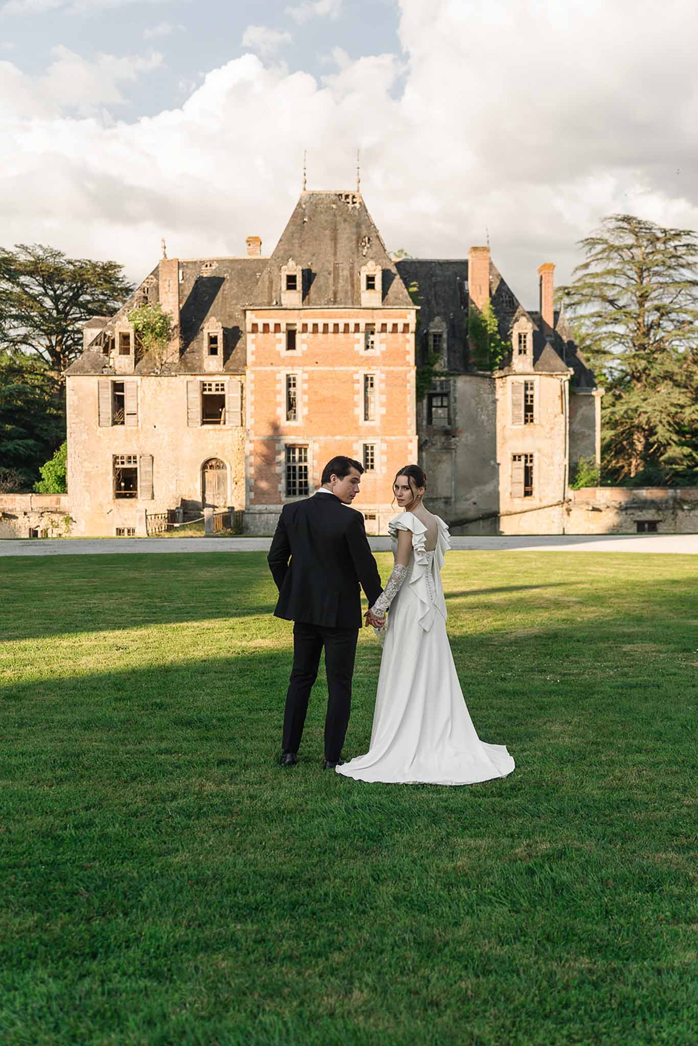 Bride and groom from behind walking toward Renaissance brick chateau in golden hour light