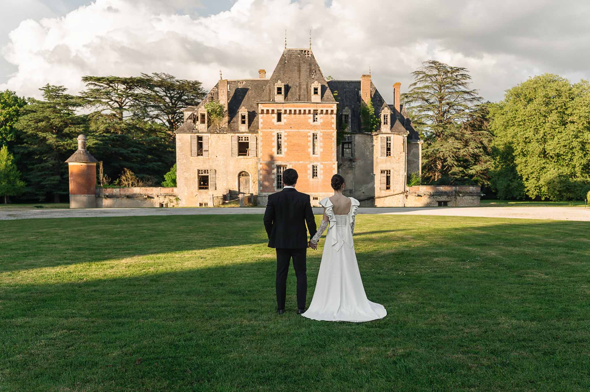 Couple from behind walking toward Loire-style chateau with round tower across open lawn