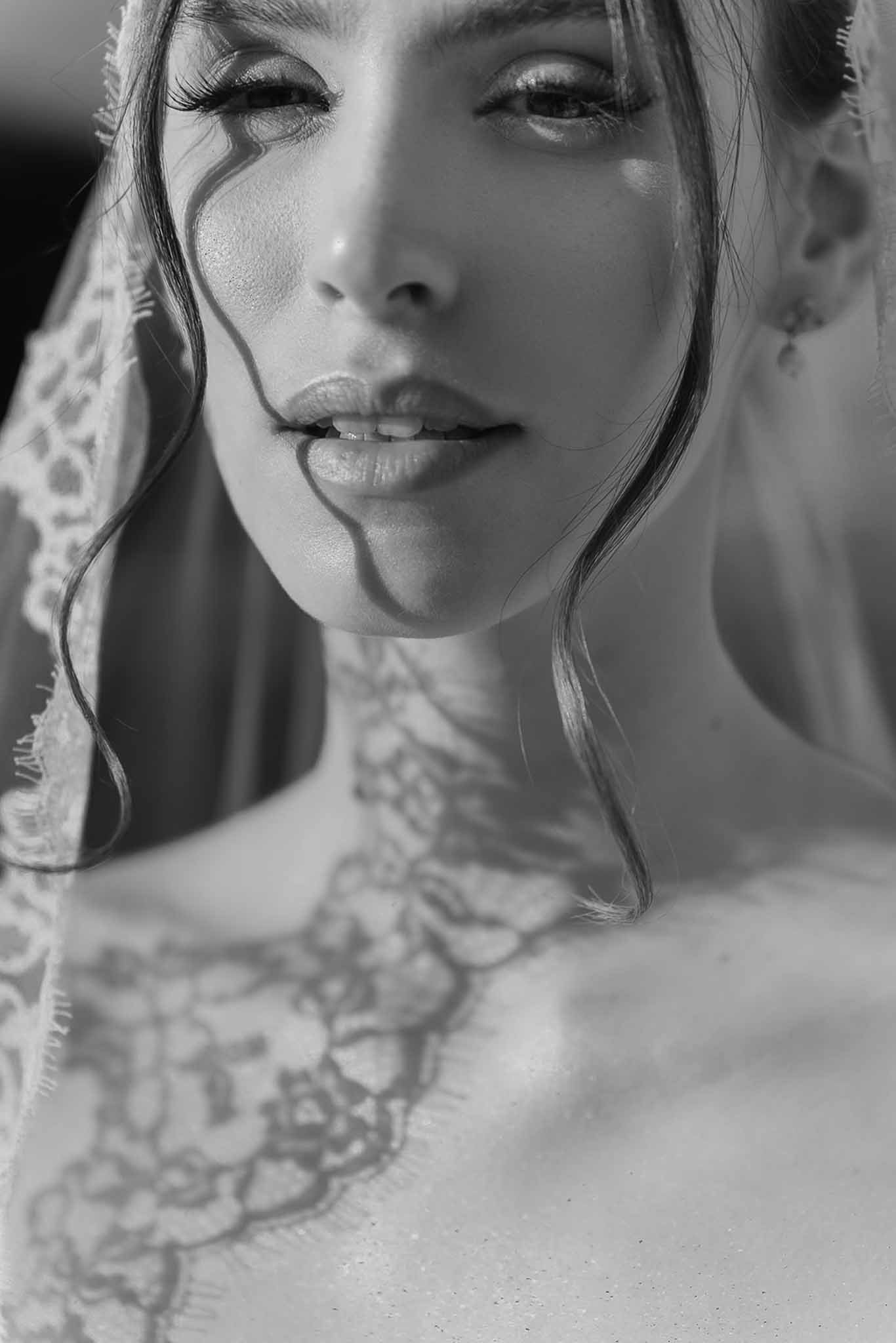 Black and white extreme close-up of bride through lace veil with floral neckline and drop earrings