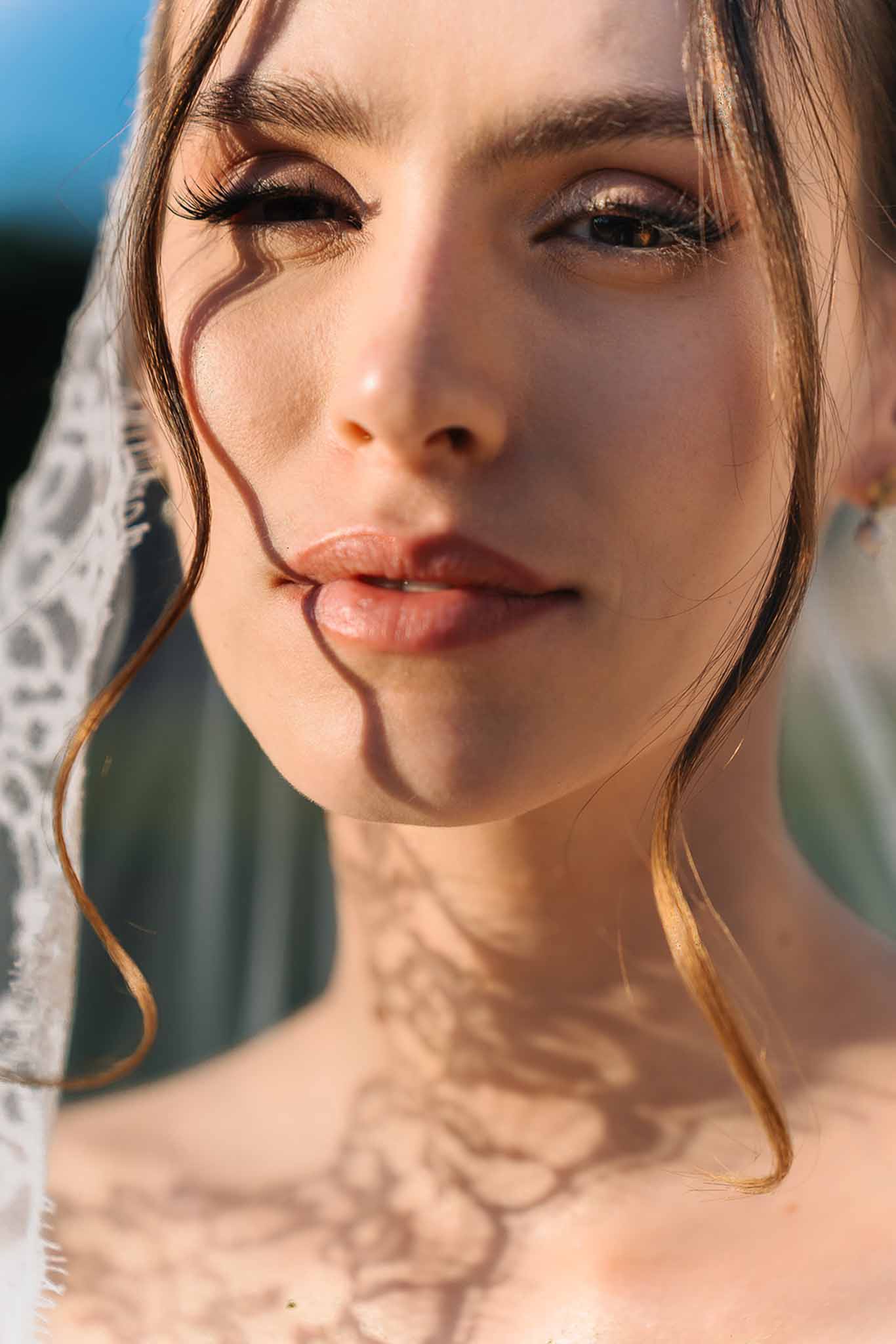Close-up portrait of bride with lace-edged veil and smoky eye makeup with lace shadow patterns on skin in sunlight