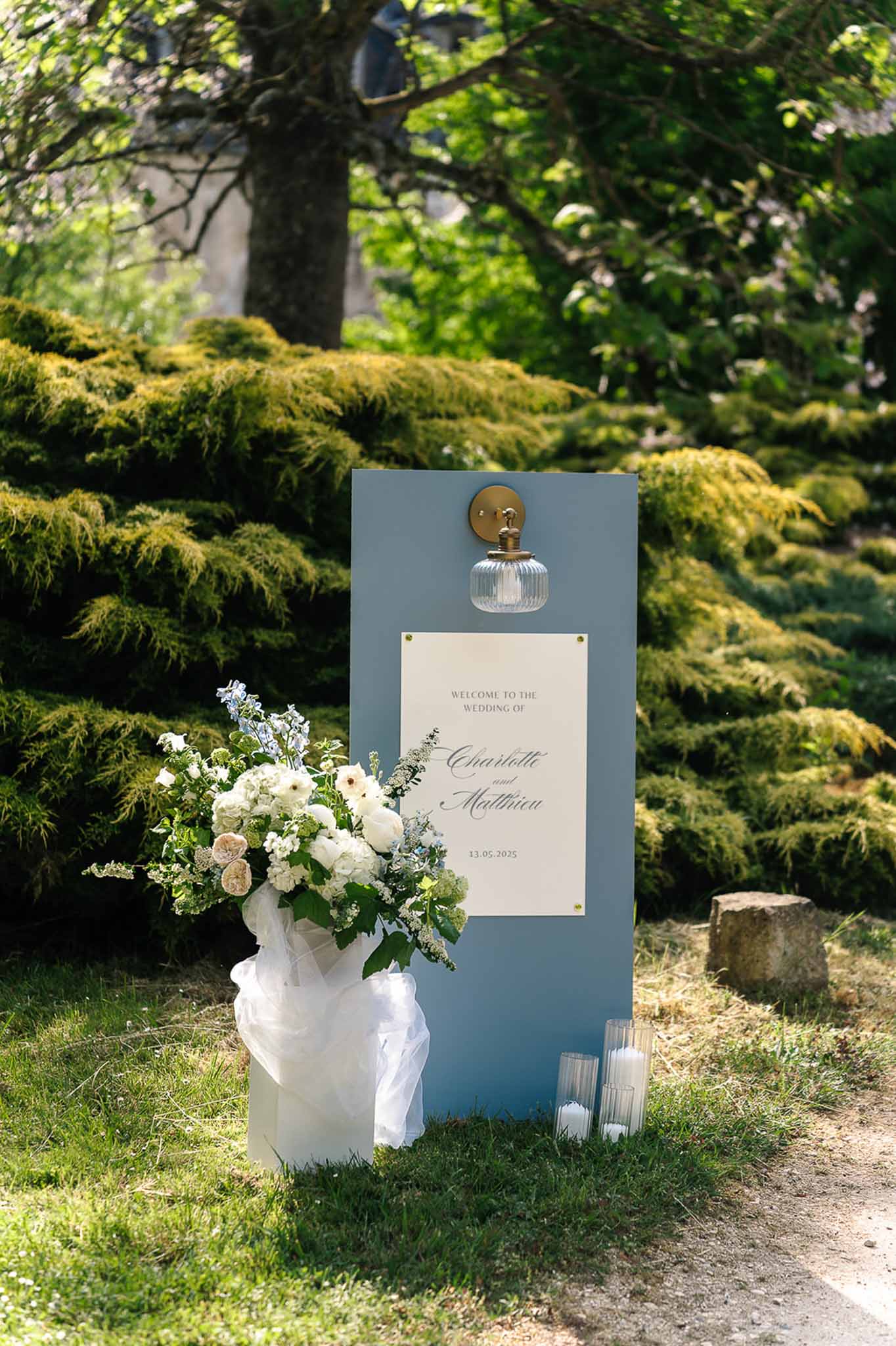 Dusty blue welcome sign with brass sconce white rose and delphinium arrangement and candle cylinders