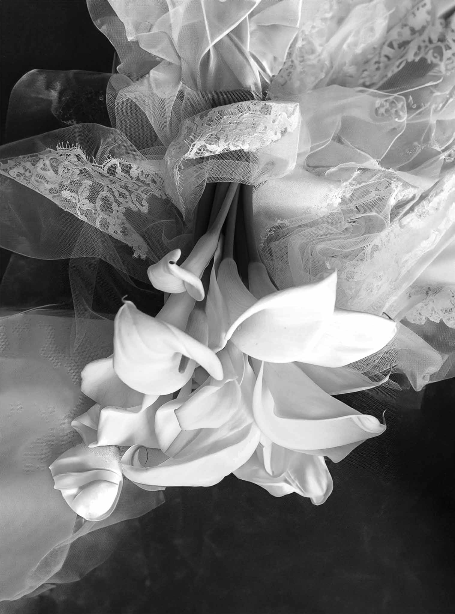 Black and white overhead shot of calla lily bouquet on lace and tulle wedding dress fabric