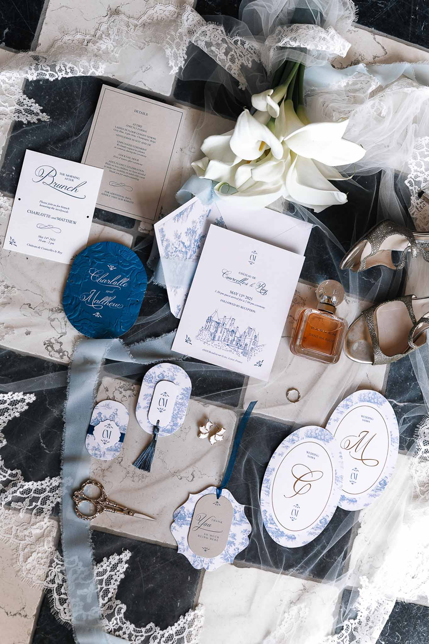 Wedding stationery suite in blue toile de Jouy with calla lilies, tulle veil, silver heels, and perfume on dark marble
