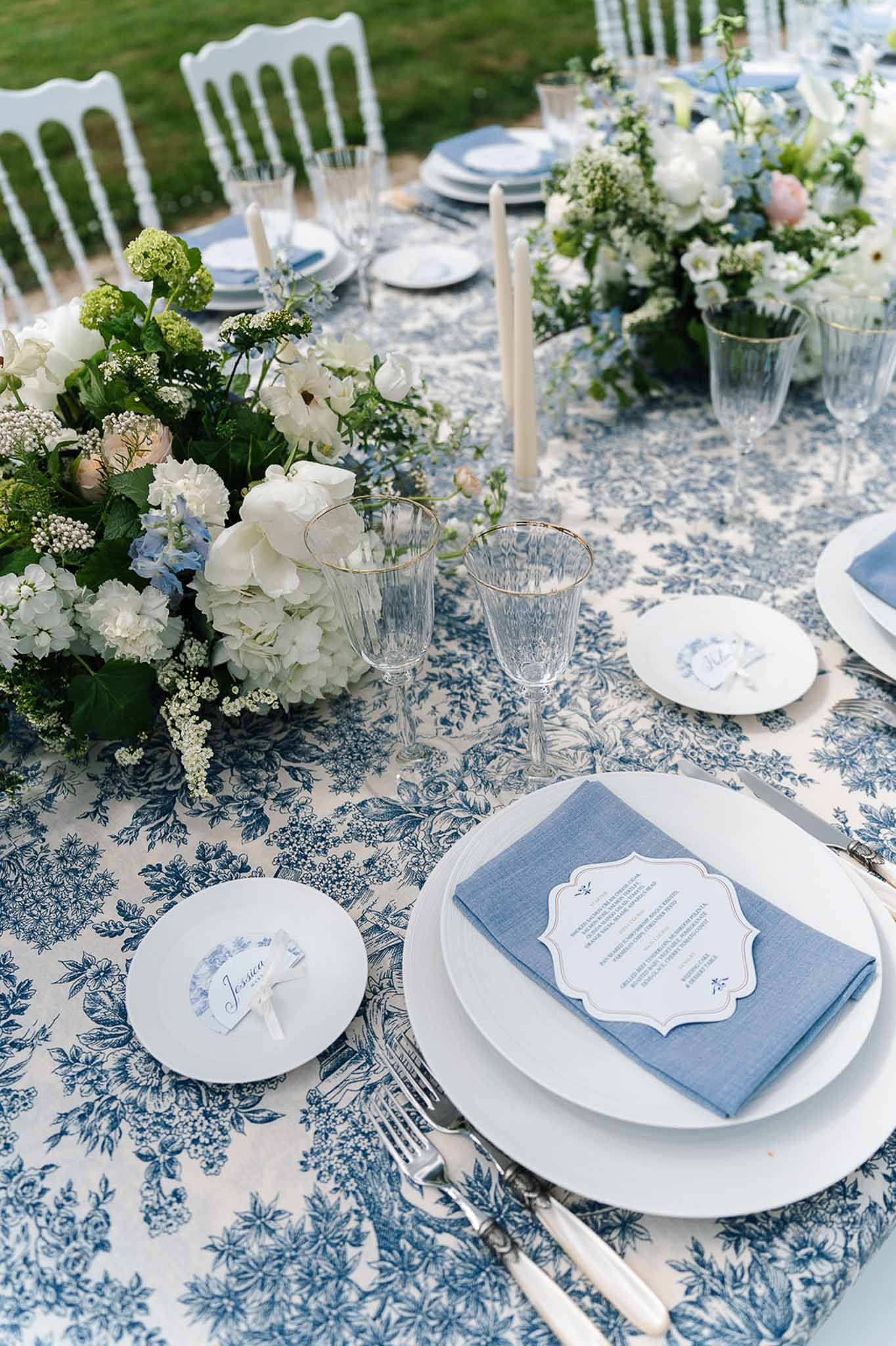 Blue toile tablecloth with white hydrangea and blush peony runner, gold-rim glasses, and ivory tapers
