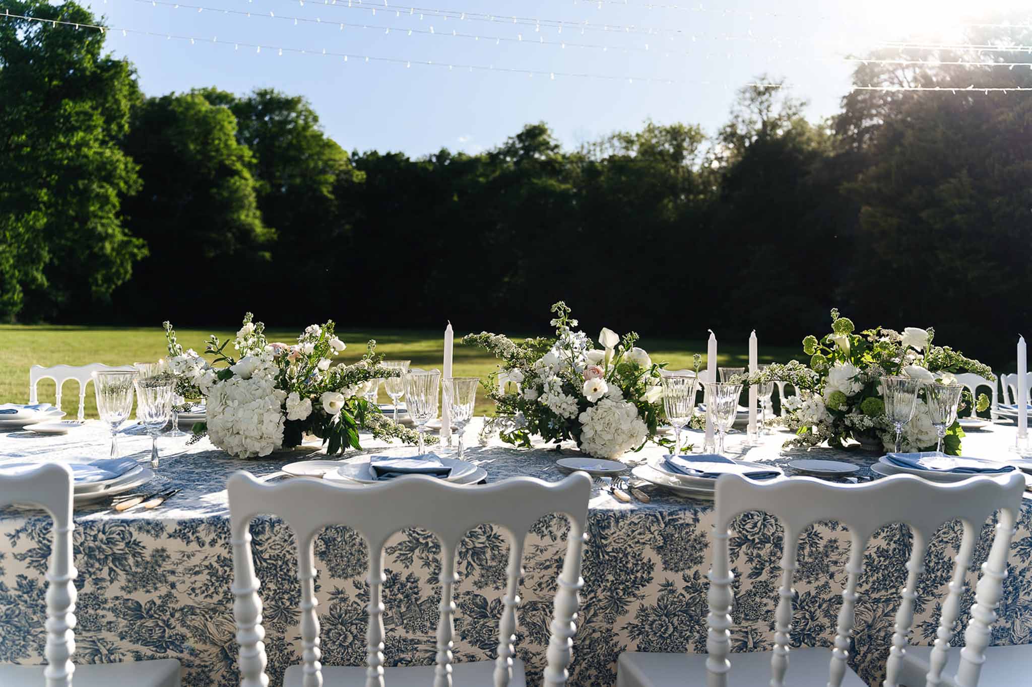 Garden reception table with navy toile tablecloth white hydrangea centerpieces gold flatware and taper candles