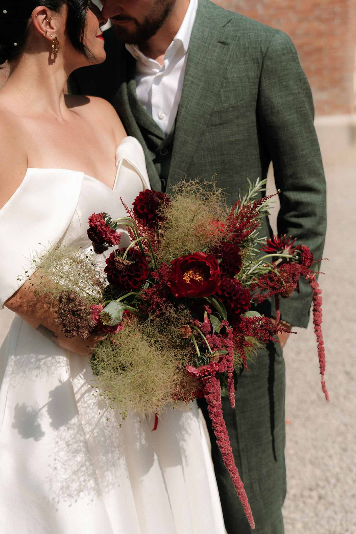 Close-up of bride and groom with large burgundy peony and red scabiosa bouquet with trailing amaranthus