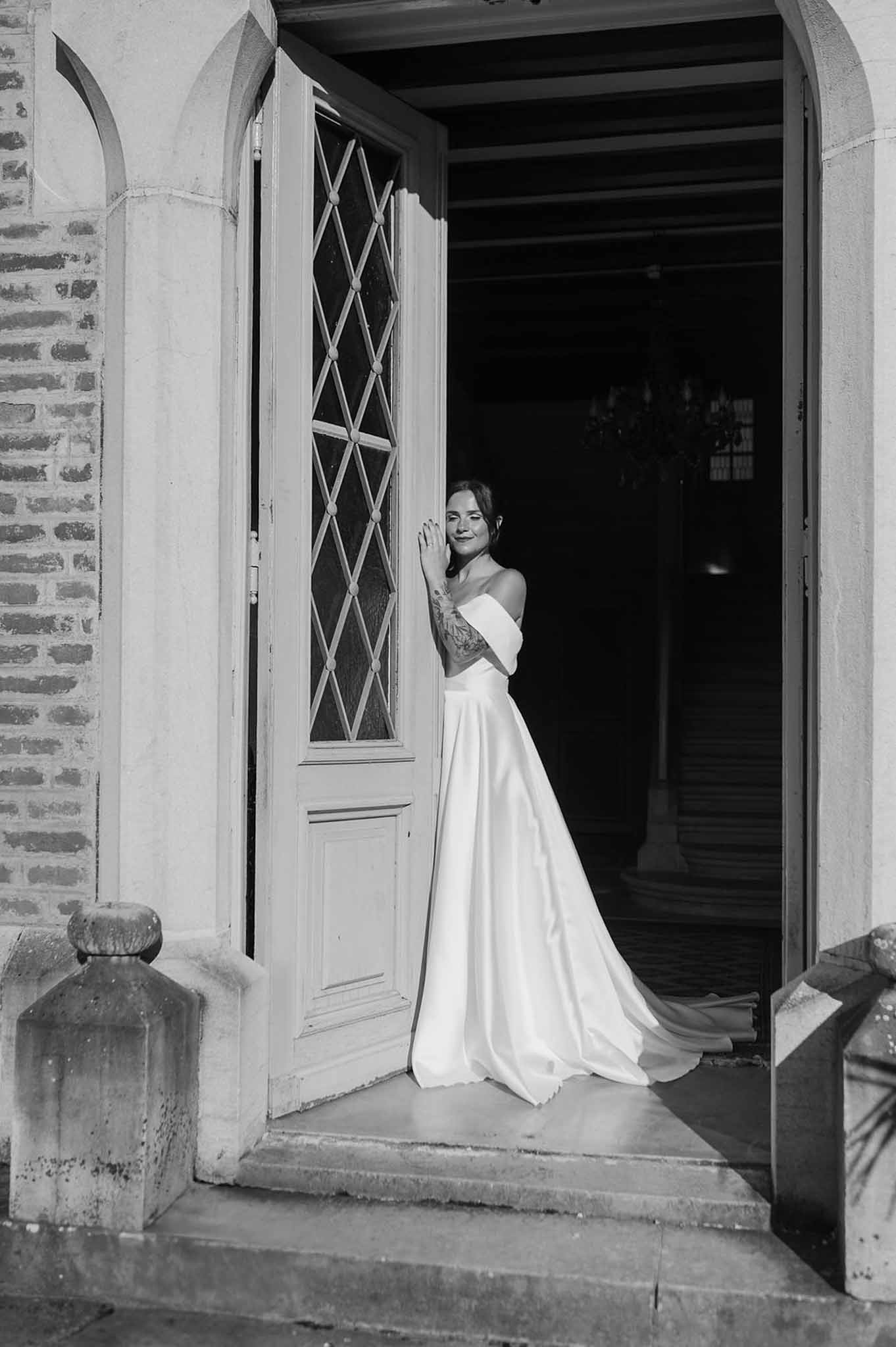 Black-and-white bridal portrait in chateau doorway with arched leaded glass doors and stone entrance