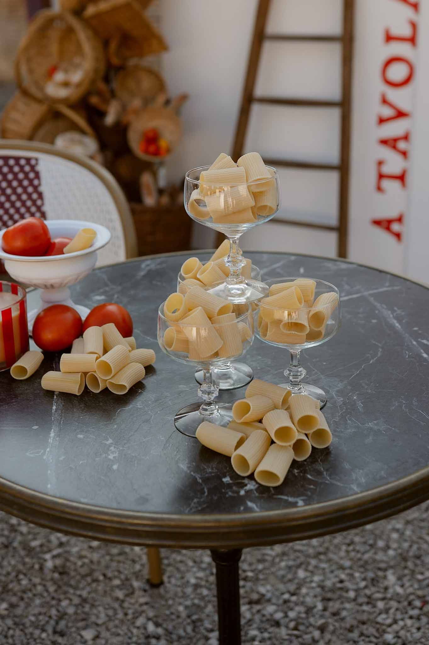 Italian-themed food station with rigatoni in glass coupes, tomatoes, and A Tavola sign on bistro table