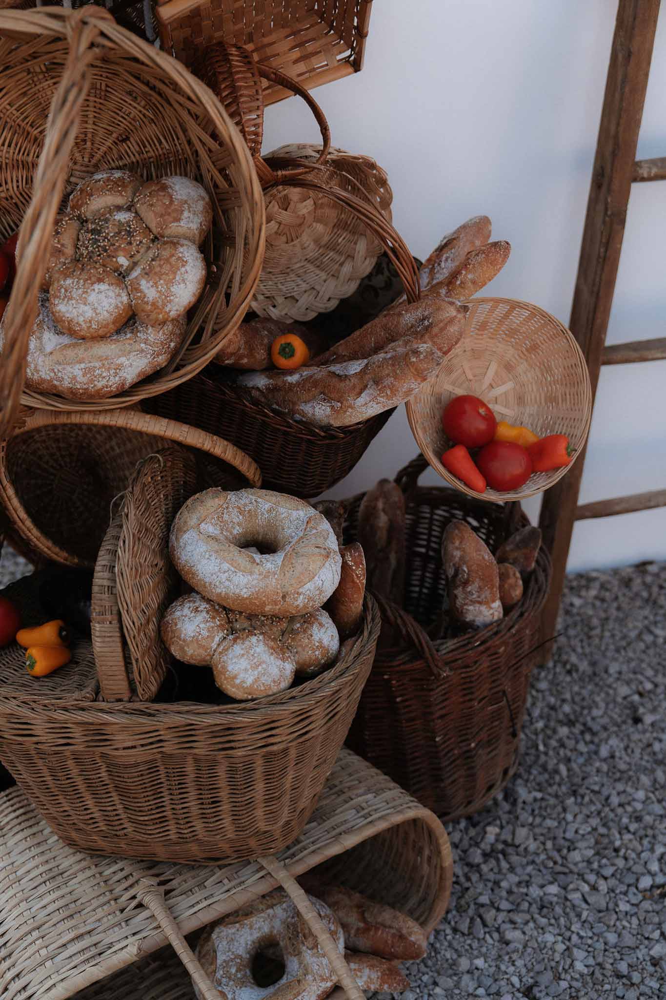 Rustic bread display in wicker baskets with artisan loaves, cherry tomatoes, and coloured peppers on gravel