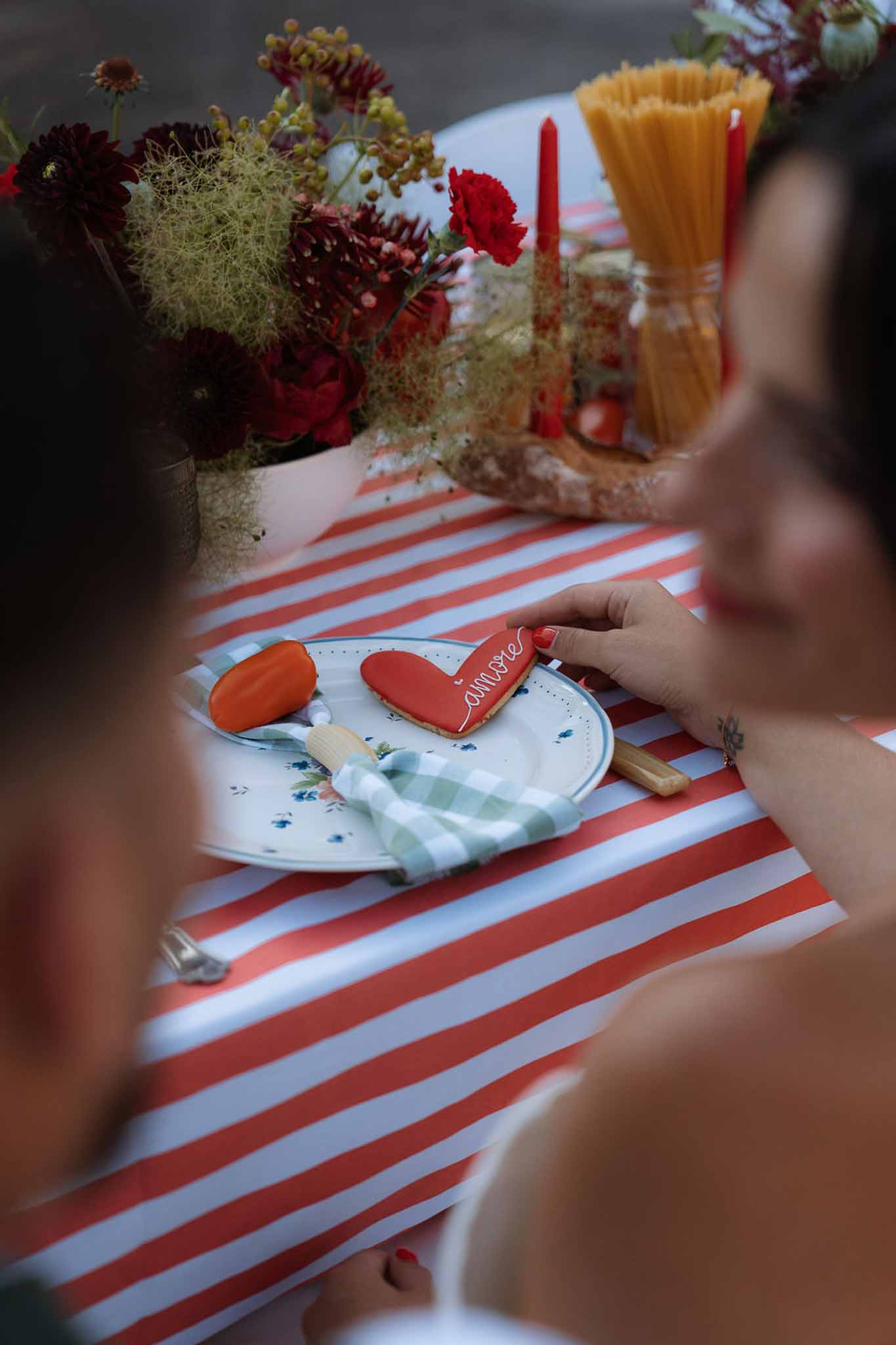 Italian-themed place setting with amore cookie, red stripe cloth, and spaghetti jar beside ranunculus
