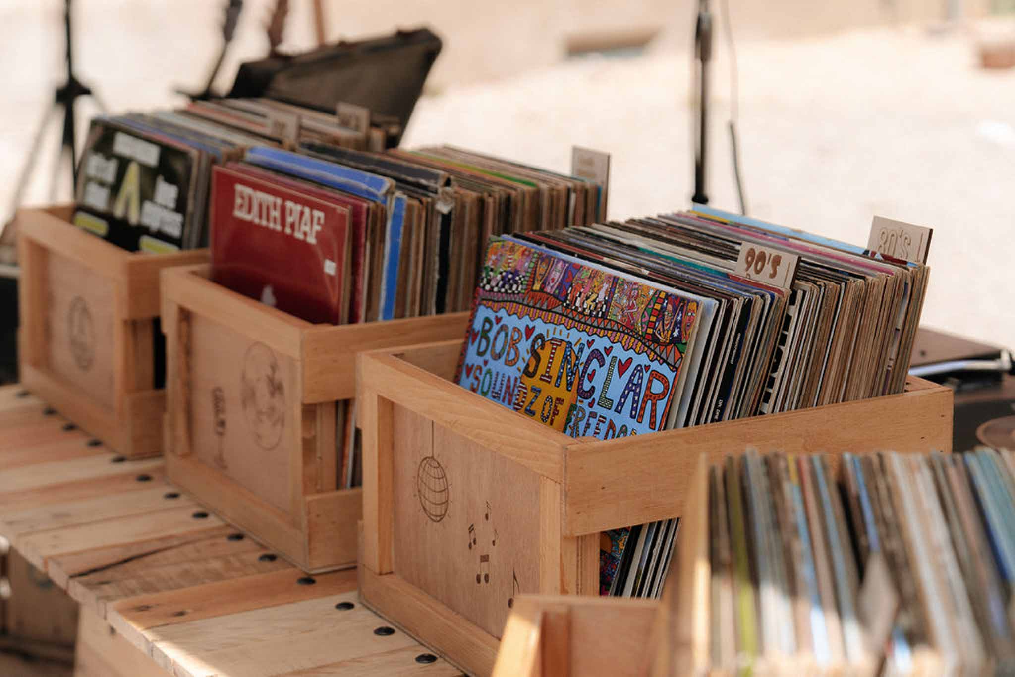 Vinyl record display station with wooden crates labelled by era Edith Piaf sleeve and DJ equipment behind