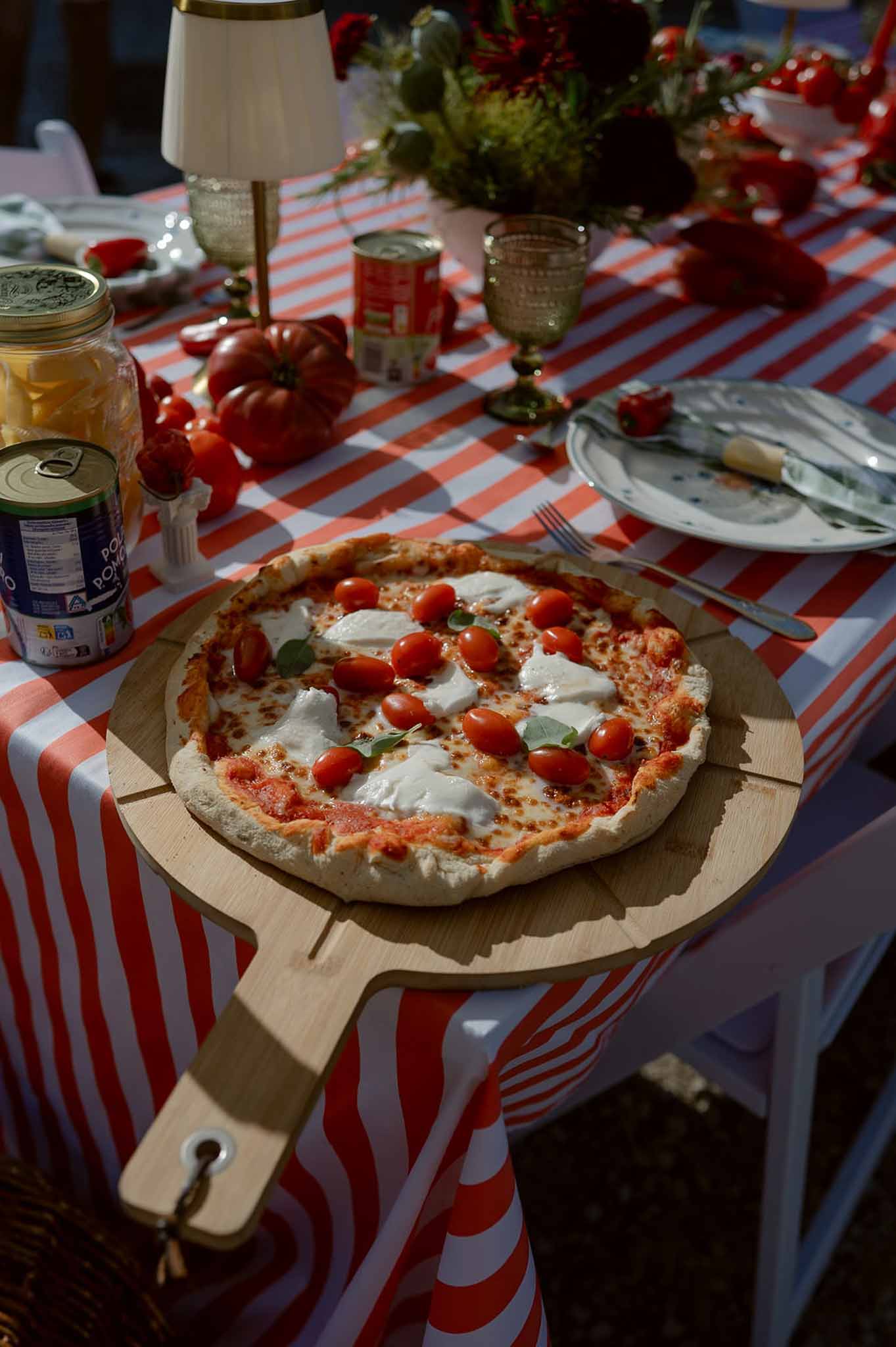 Pizza on wood peel with burrata and basil on red and white striped tablecloth in Italian trattoria-style reception