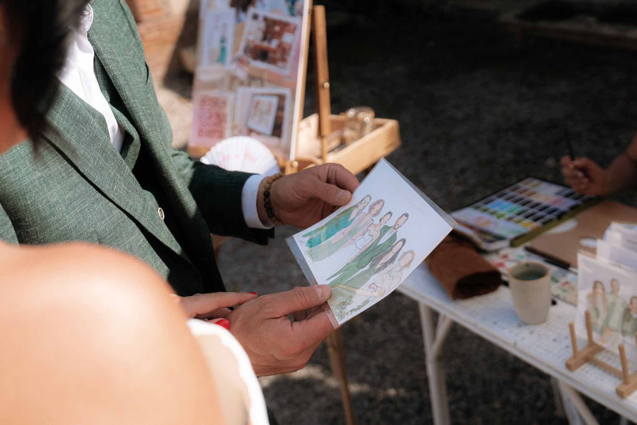 Guests holding watercolor portrait from live illustrator station at wedding cocktail hour