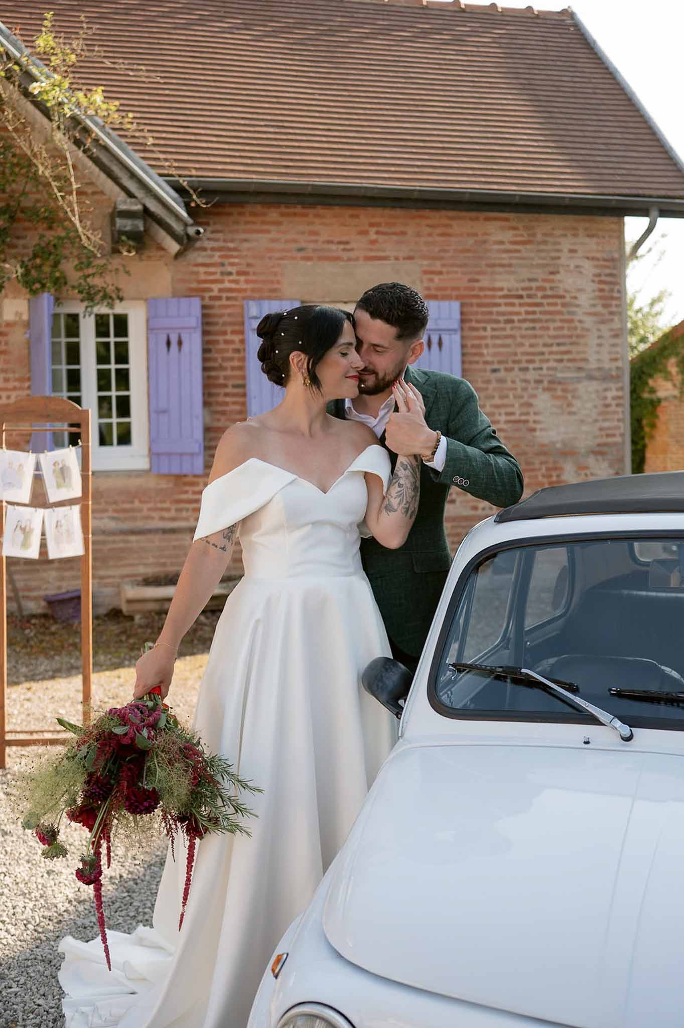 Tattooed bride with burgundy dahlia bouquet and groom in green check jacket beside vintage Fiat 500