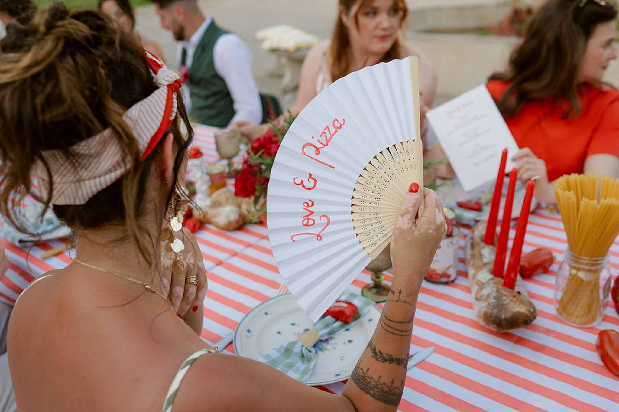 Love and Pizza fan on red-striped table with spaghetti jars, red carnations, and brass candleholders