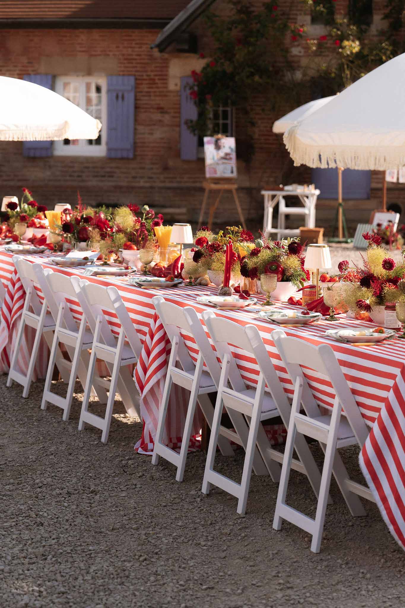 Red and white striped tablecloth with crimson dahlias gold candlesticks amber glasses and white parasols