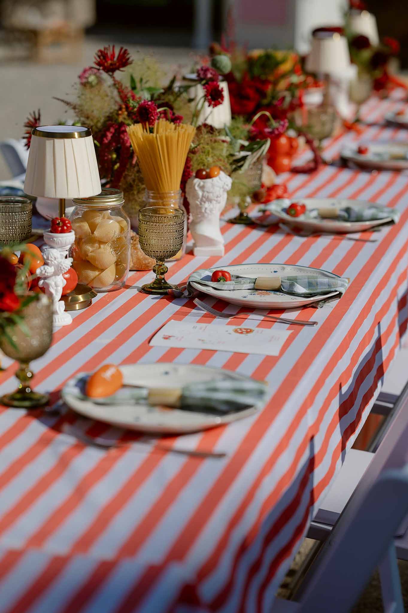 Italian trattoria-themed table with red stripe linen, crimson dahlias, pasta jars, and cherry tomatoes