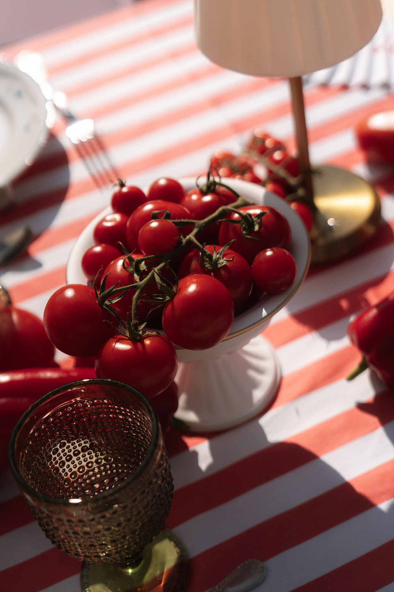 Cherry tomatoes on cake stand with red chili peppers and olive hobnail glass on red-white stripe cloth