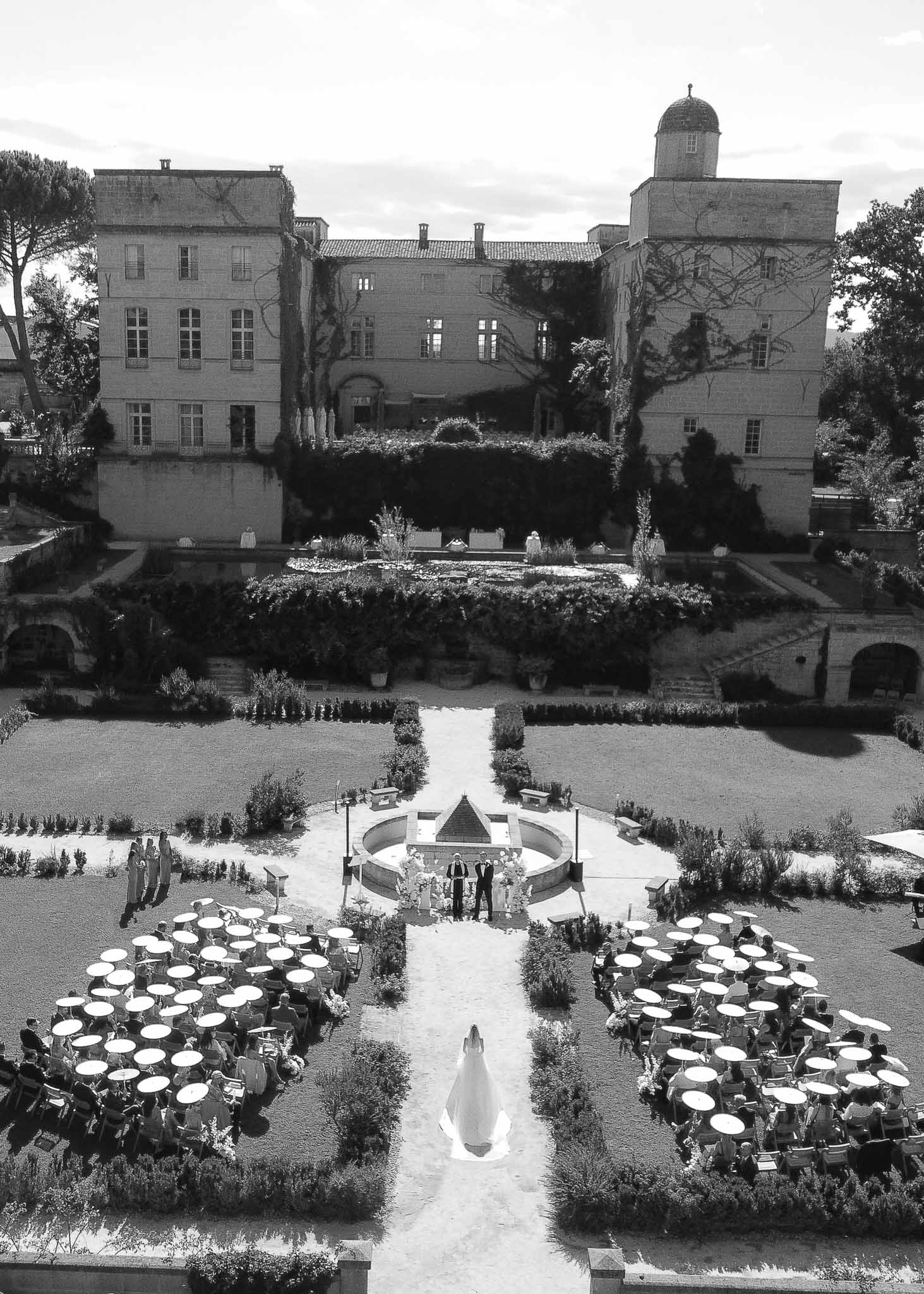 Black and white aerial shot of bride walking aisle in parterre garden toward fountain altar