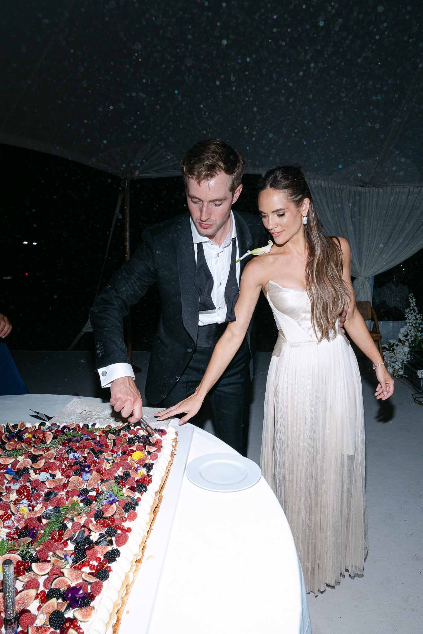 Couple cutting fig and berry sheet cake under starlight tent ceiling, bride in strapless tulle gown