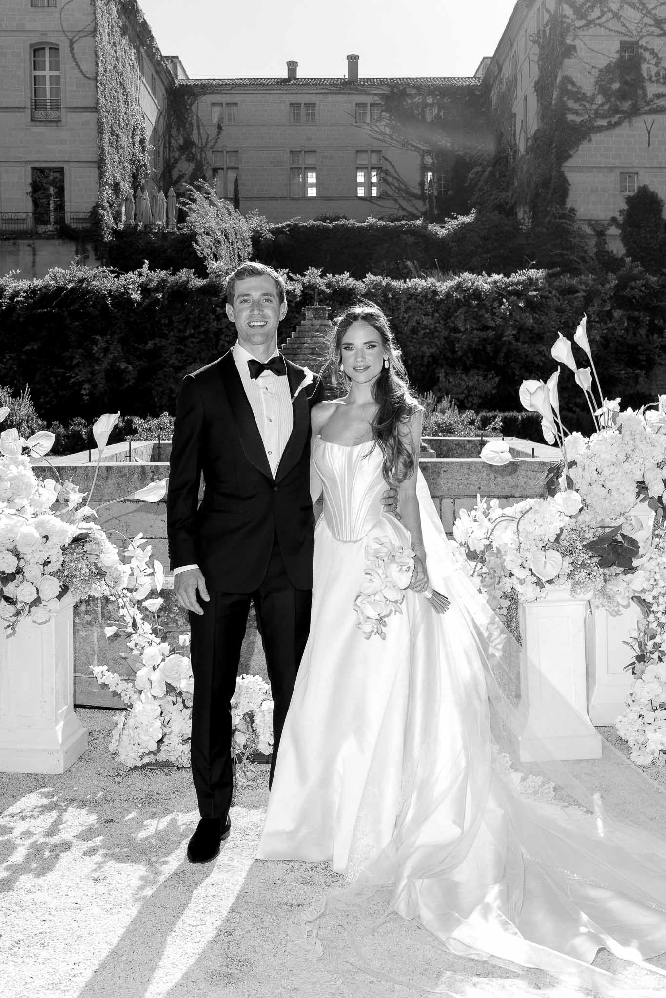 Black and white couple at ceremony altar flanked by anthurium and hydrangea pedestal arrangements before chateau