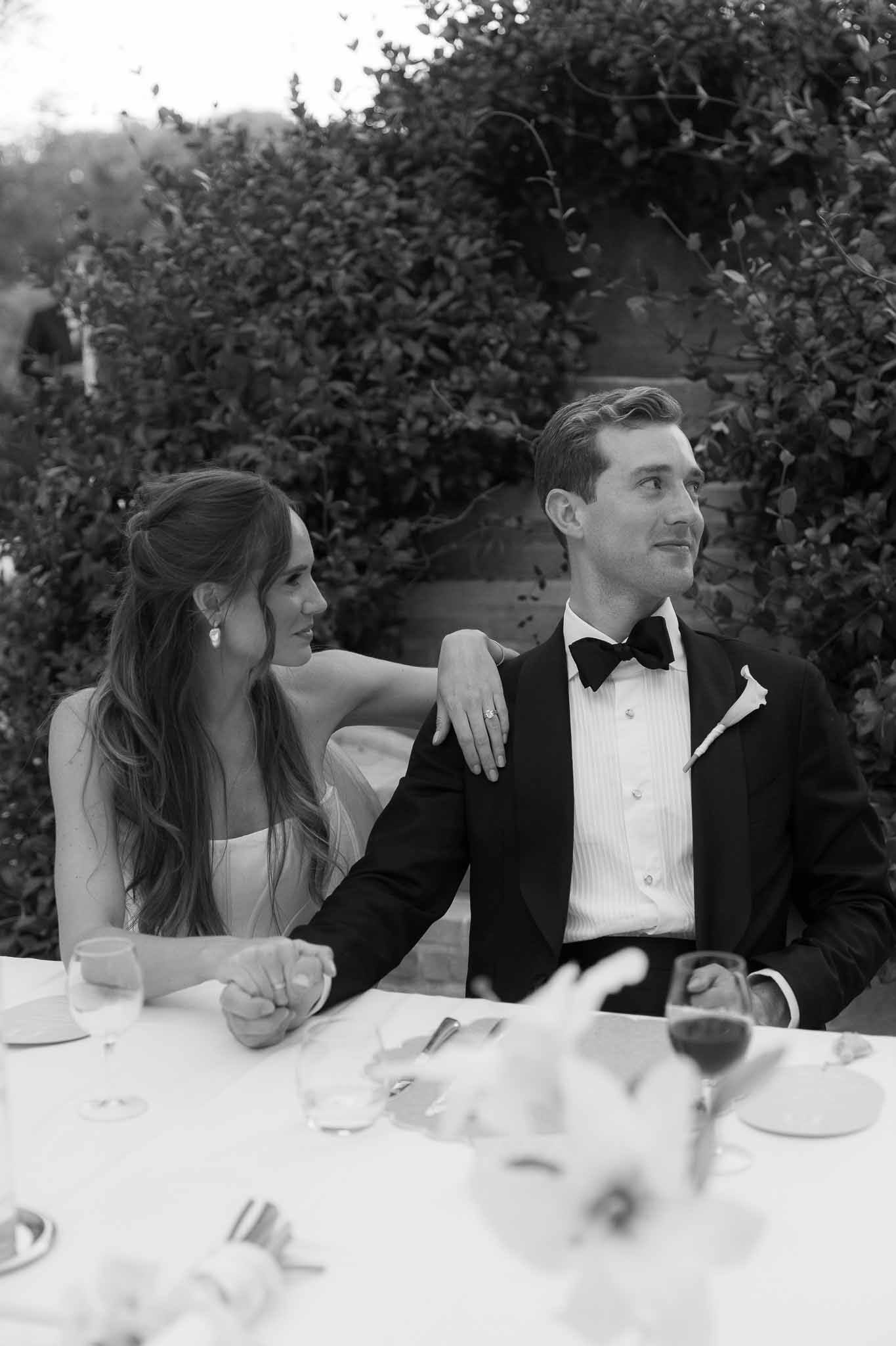 Black and white portrait of bride and groom seated at reception table during outdoor speeches