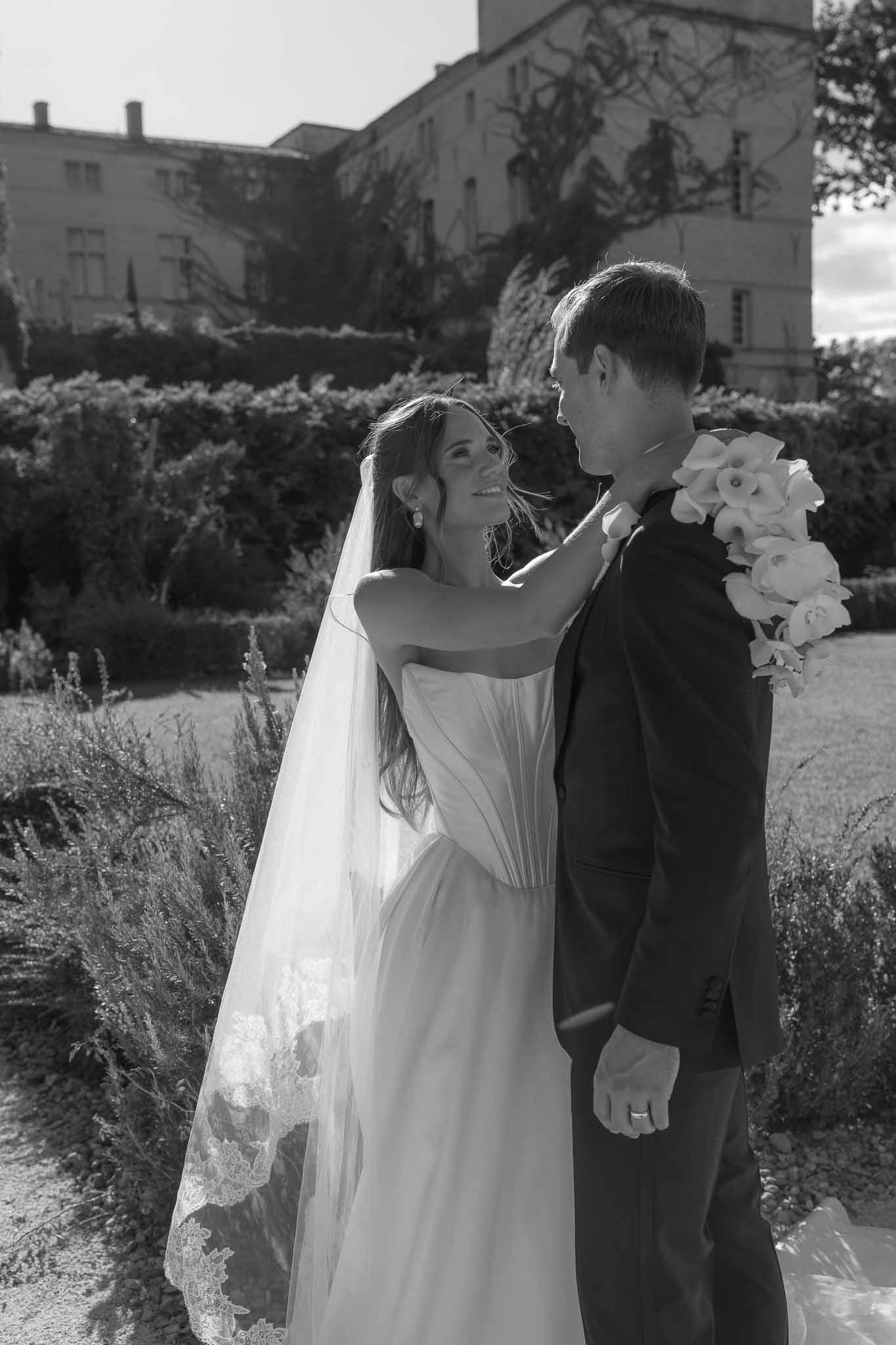 Black and white couple portrait in formal garden with cathedral lace-trimmed veil and chateau beyond